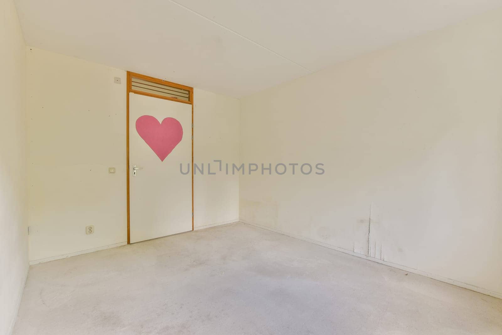 An empty interior space featuring a door adorned with a pink heart design. The walls are neutral and the floor is bare, creating a minimalist vibe.