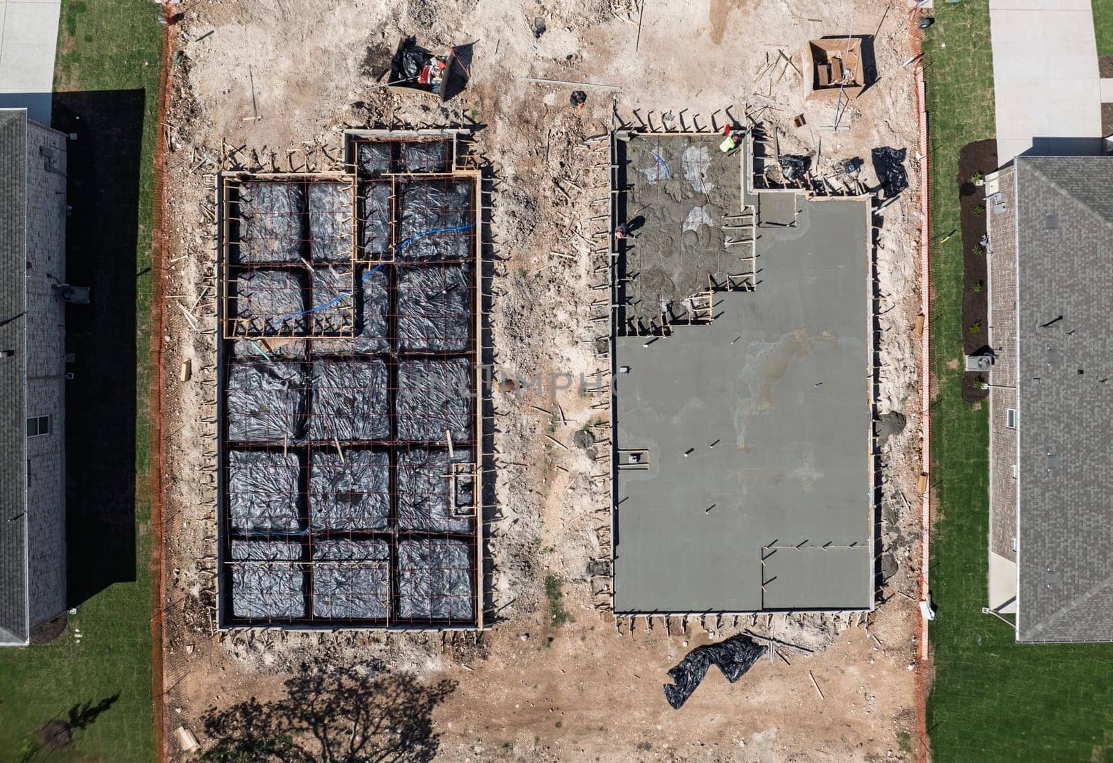Overhead view of two construction sites, one with a concrete slab and the other a framed foundation ready for concrete