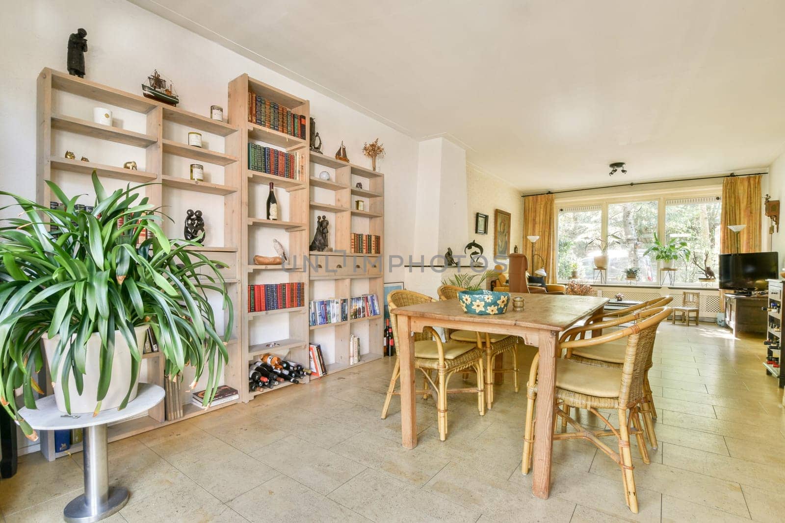 A beautifully arranged dining area featuring natural light, a wooden dining table, elegant chairs, and an eye-catching bookshelf filled with decor items.