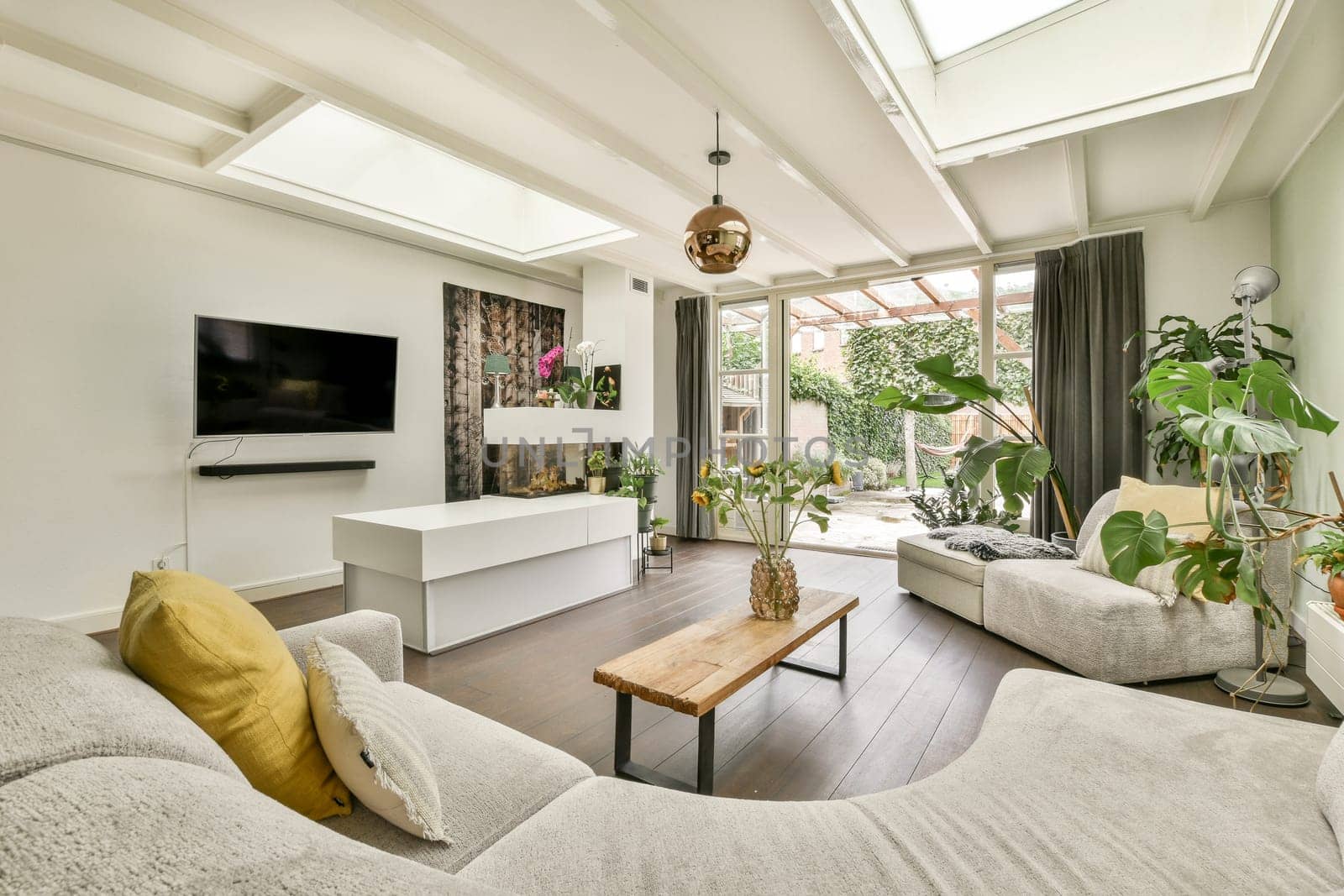 A spacious and bright modern living room featuring large windows, vibrant plants, and contemporary furniture that creates a welcoming atmosphere.