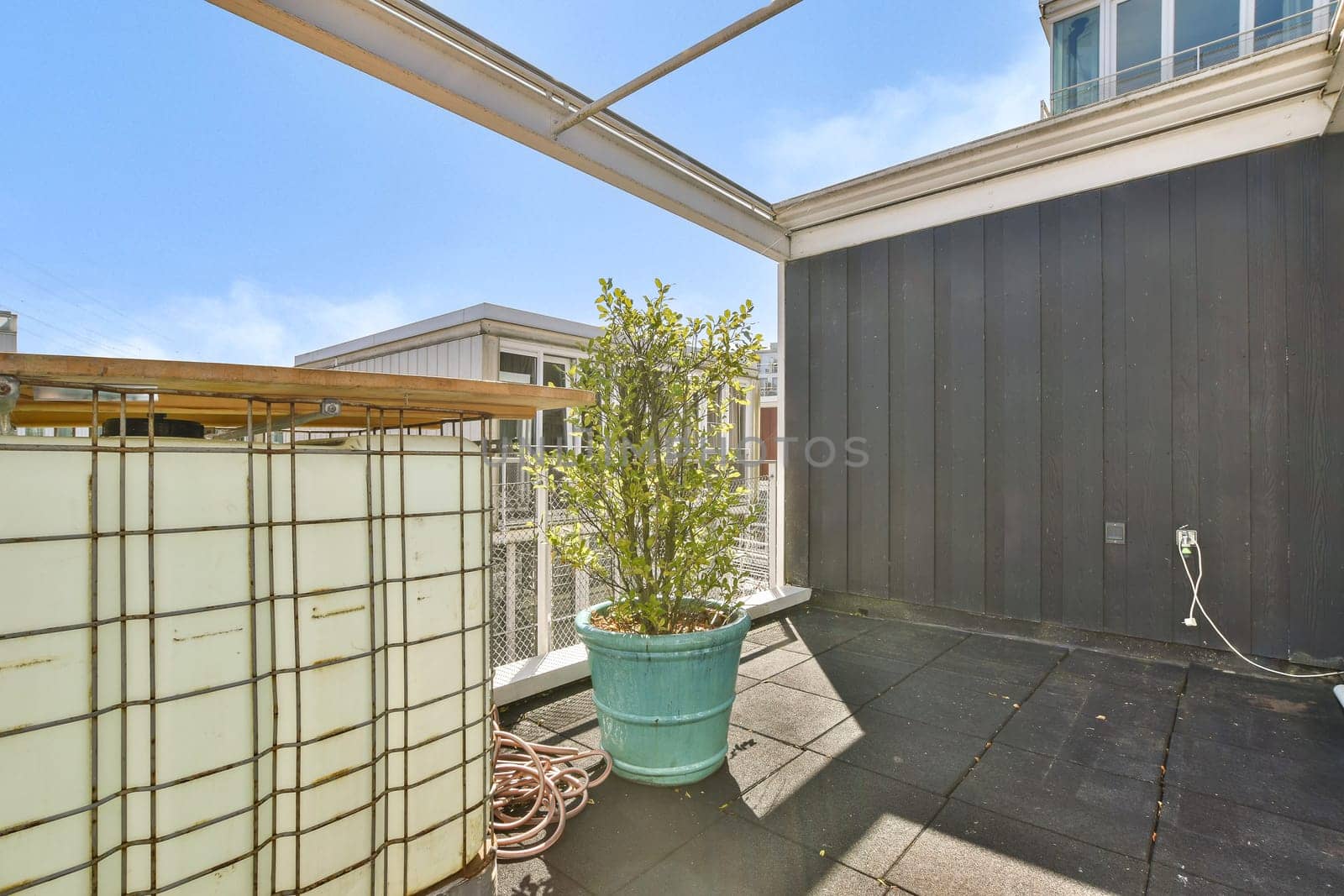 A sleek modern terrace showcasing a potted plant against a stylish architectural background, complemented by a clear blue sky and natural light.