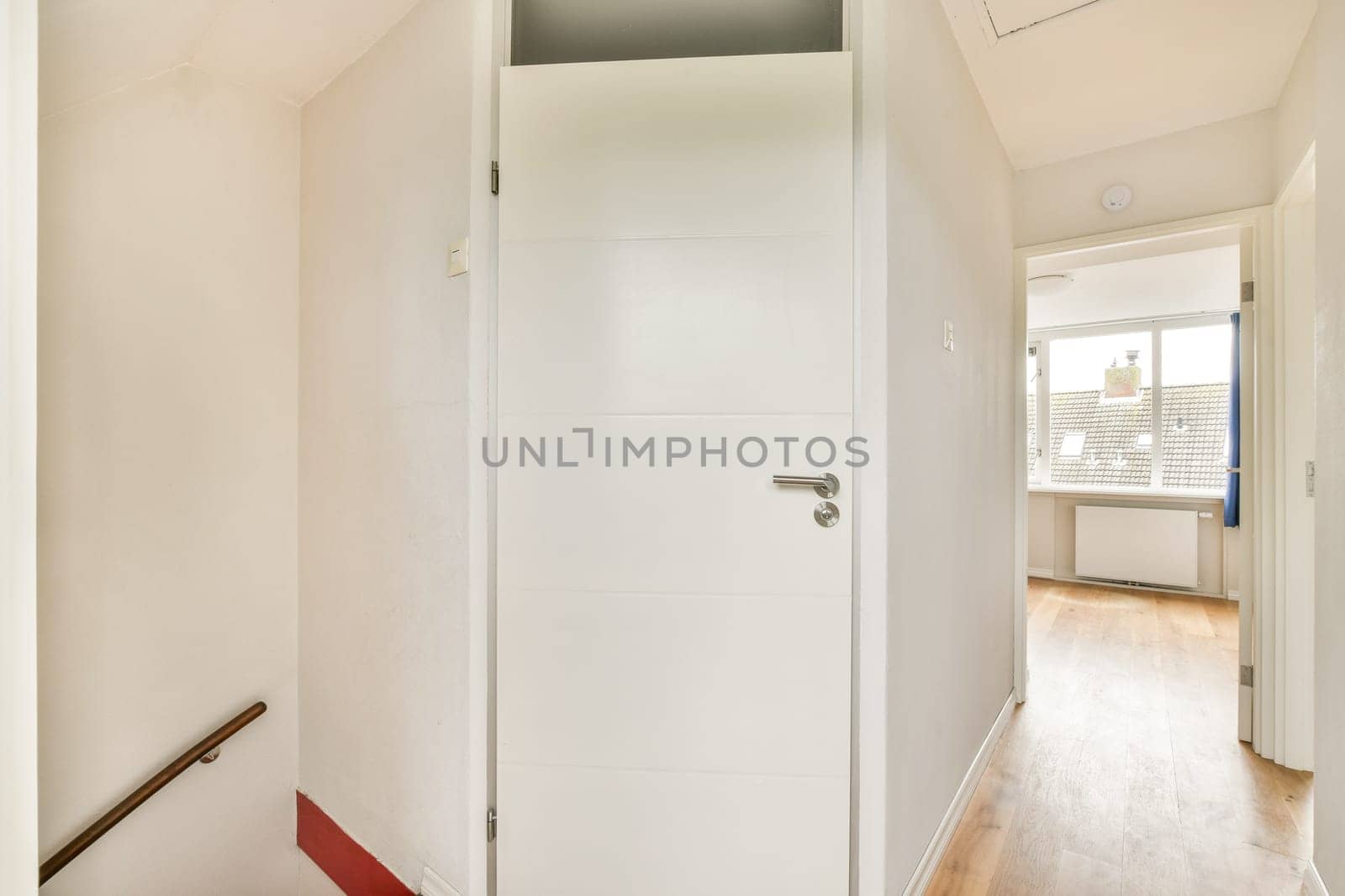 A clean, modern interior hallway featuring a white door and light wooden flooring, creating a bright and inviting atmosphere in the living space.