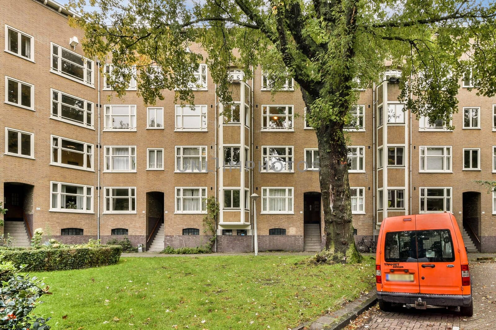 A contemporary residential structure surrounded by greenery, featuring large windows and a vibrant tree in front, showcasing urban architecture.