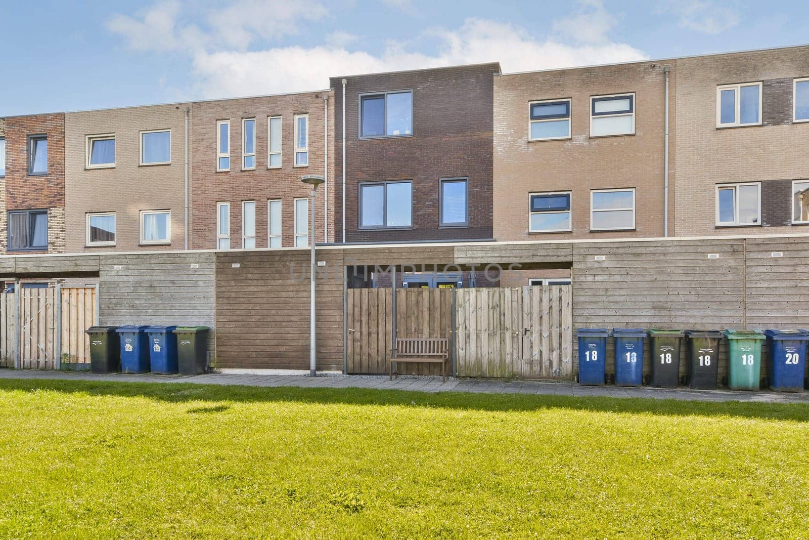 Contemporary row of residential buildings featuring colorful recycling bins in a green open area, showcasing modern architecture and eco-friendly practices.