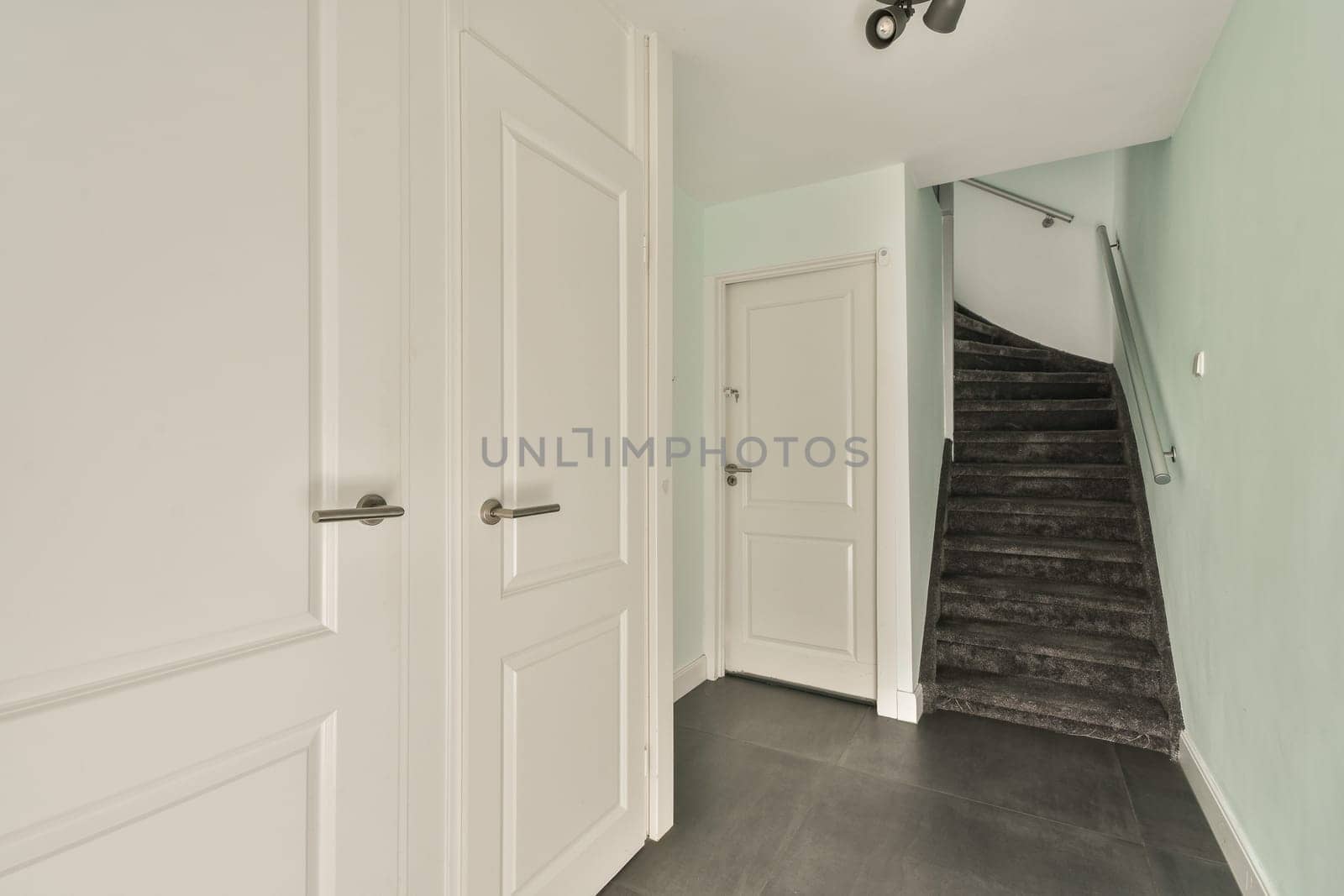 A sleek entrance featuring white doors and a modern staircase, complemented by soft green walls and dark flooring that enhances the overall ambiance.