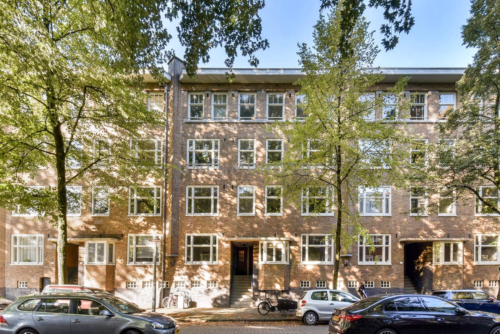 A contemporary urban apartment building surrounded by lush trees, featuring large windows and a welcoming facade in a vibrant neighborhood.