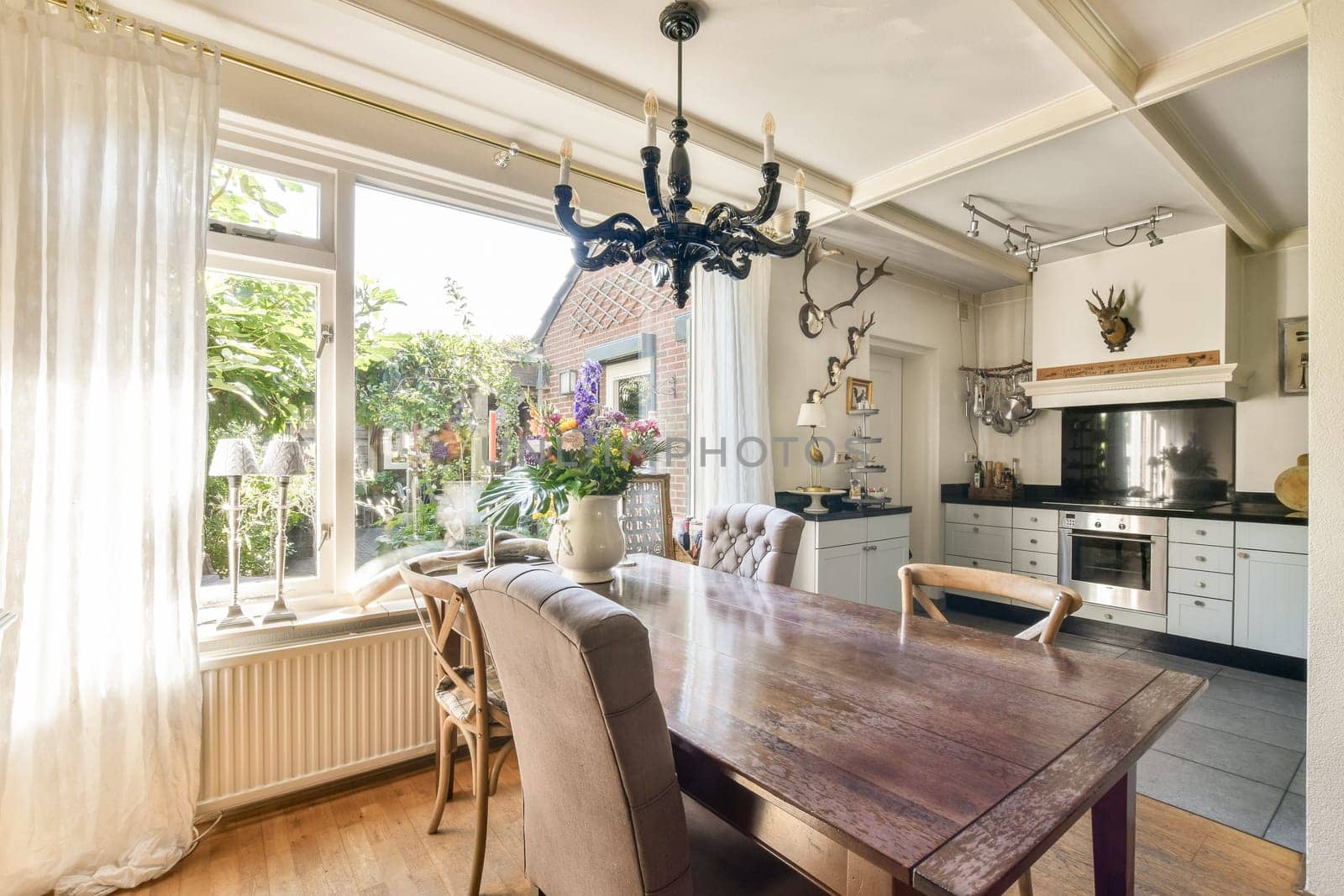 A sunlit dining area featuring a wooden table, elegant chairs, and large windows bringing in natural light, enhancing the homely ambiance.