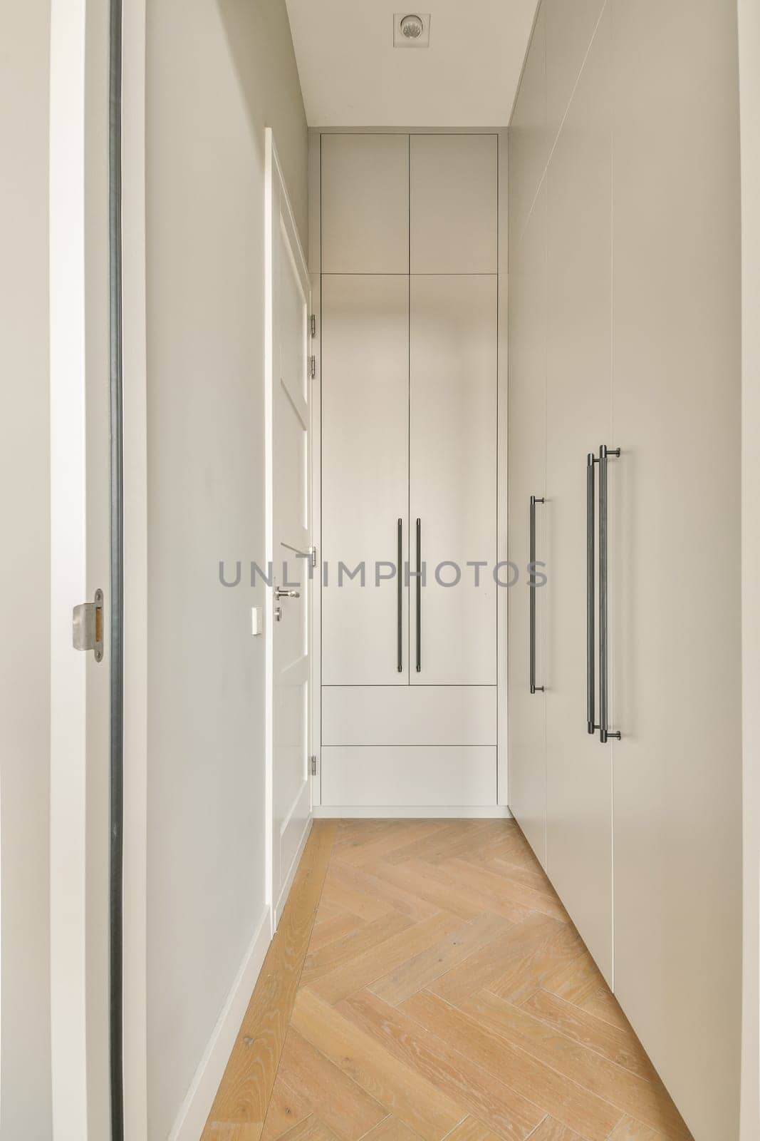A clean, modern hallway featuring sleek cabinetry and warm wooden flooring. The design emphasizes minimalism with neutral colors and straight lines.