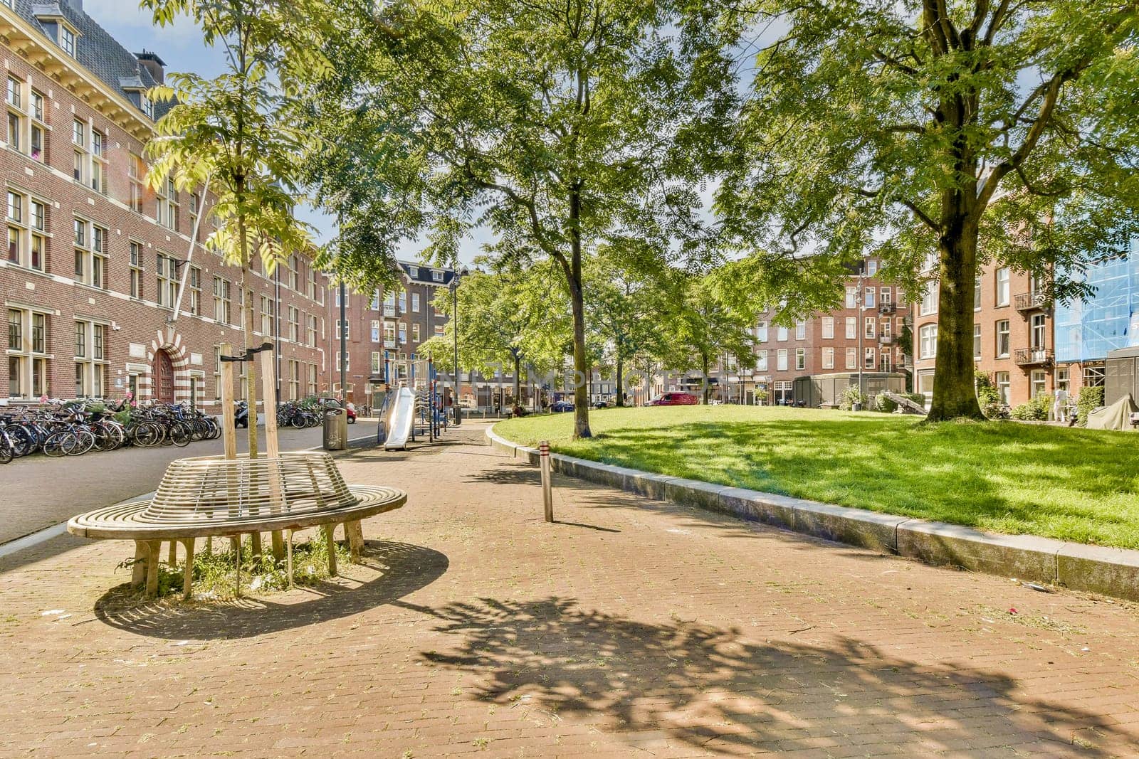 A vibrant urban park in Amsterdam features modern wooden benches surrounded by greenery and brick buildings, showcasing a blend of nature and architecture.