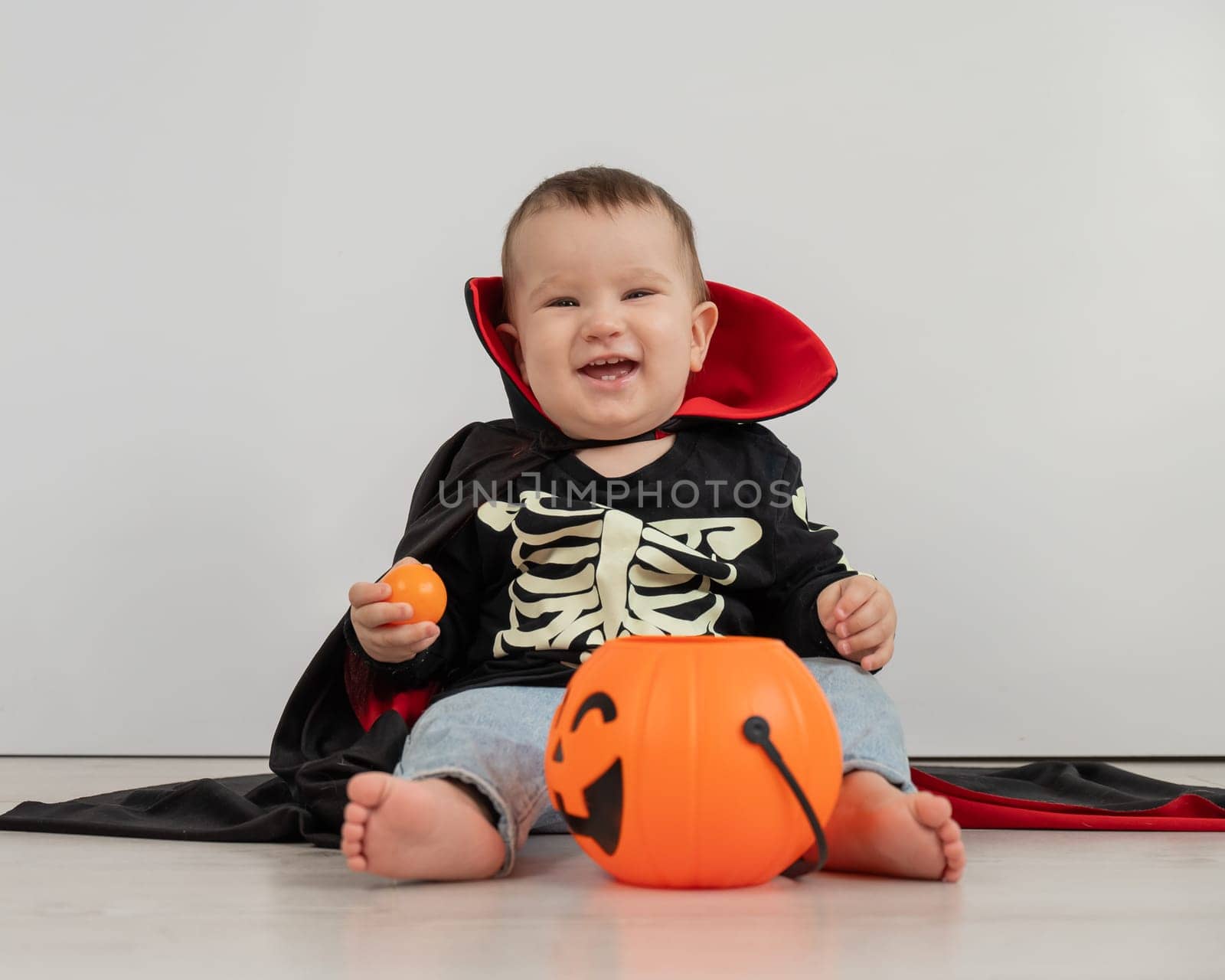 Cute caucasian boy in dracula halloween costume holding candy basket on white background