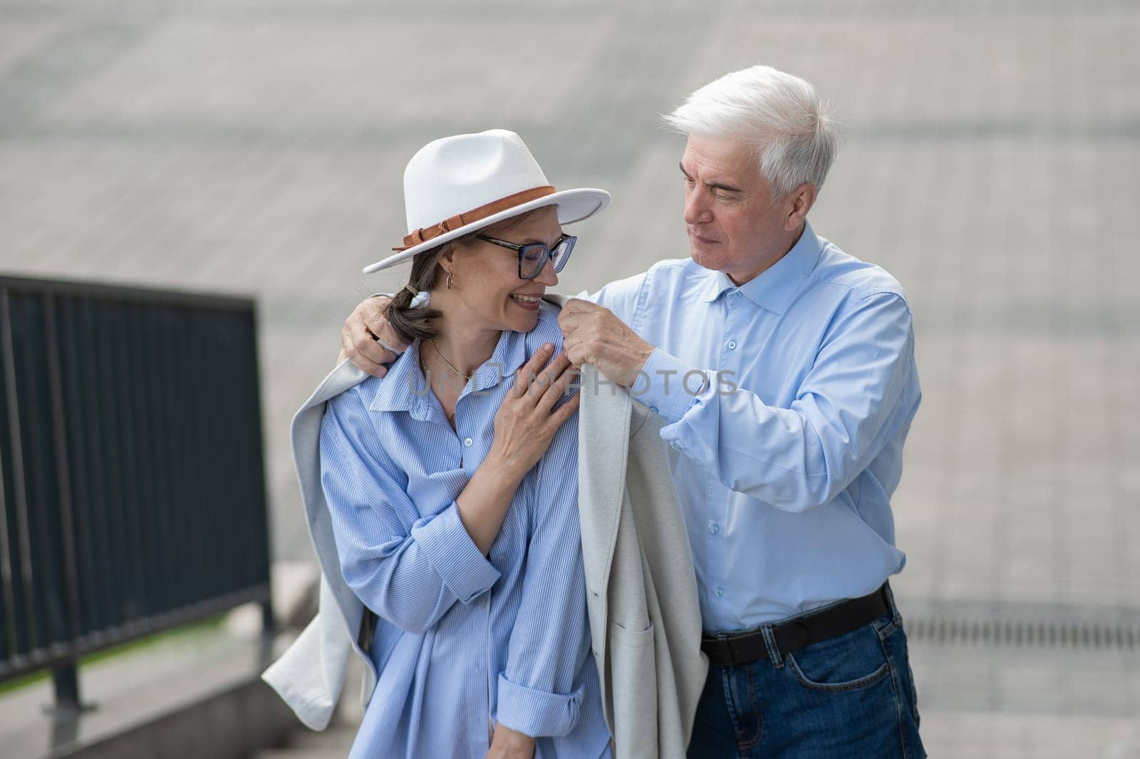 An elderly man puts his jacket on a woman. Romantic relationships of mature people