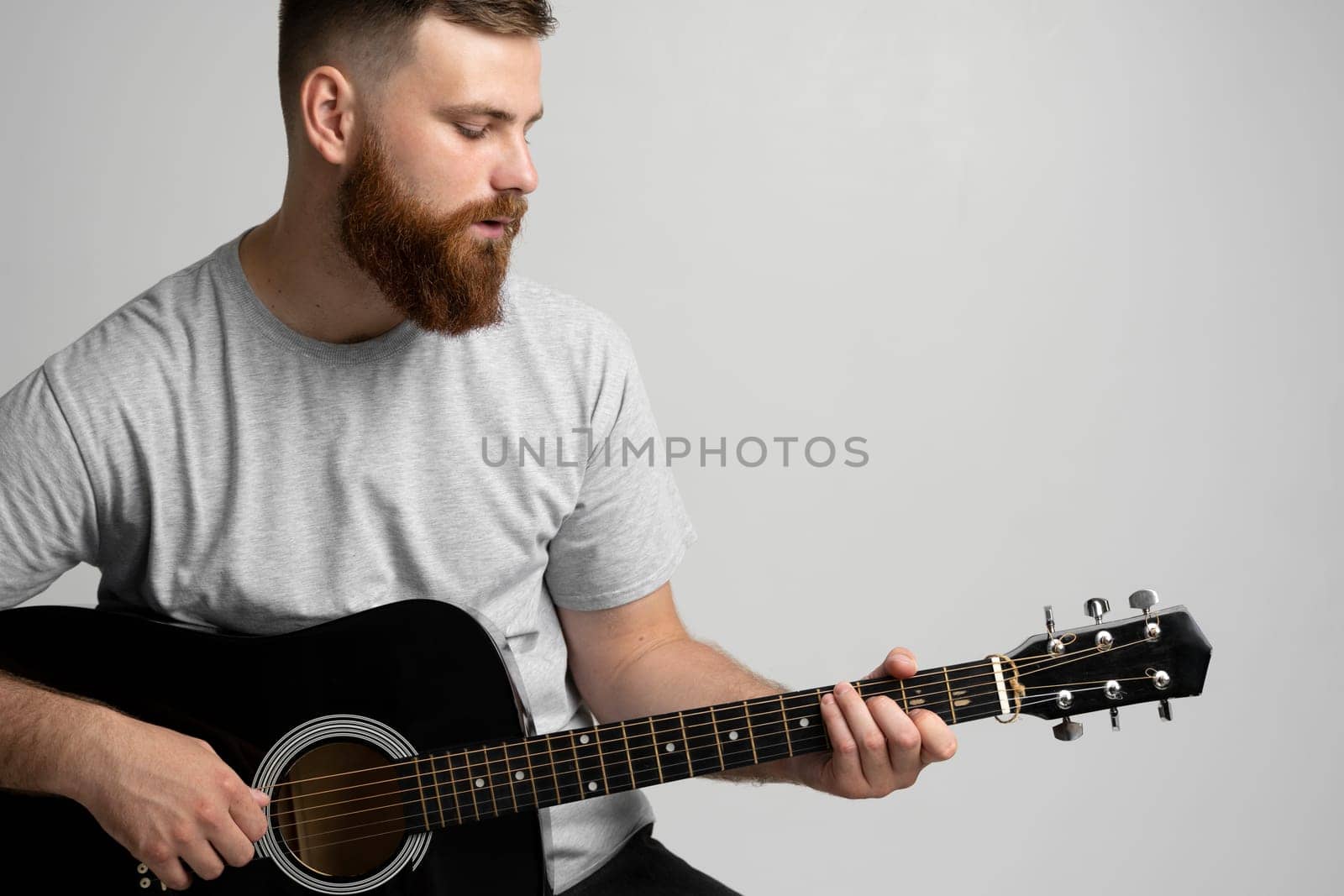 Bearded brunette man with a guitar in hands playing a song
