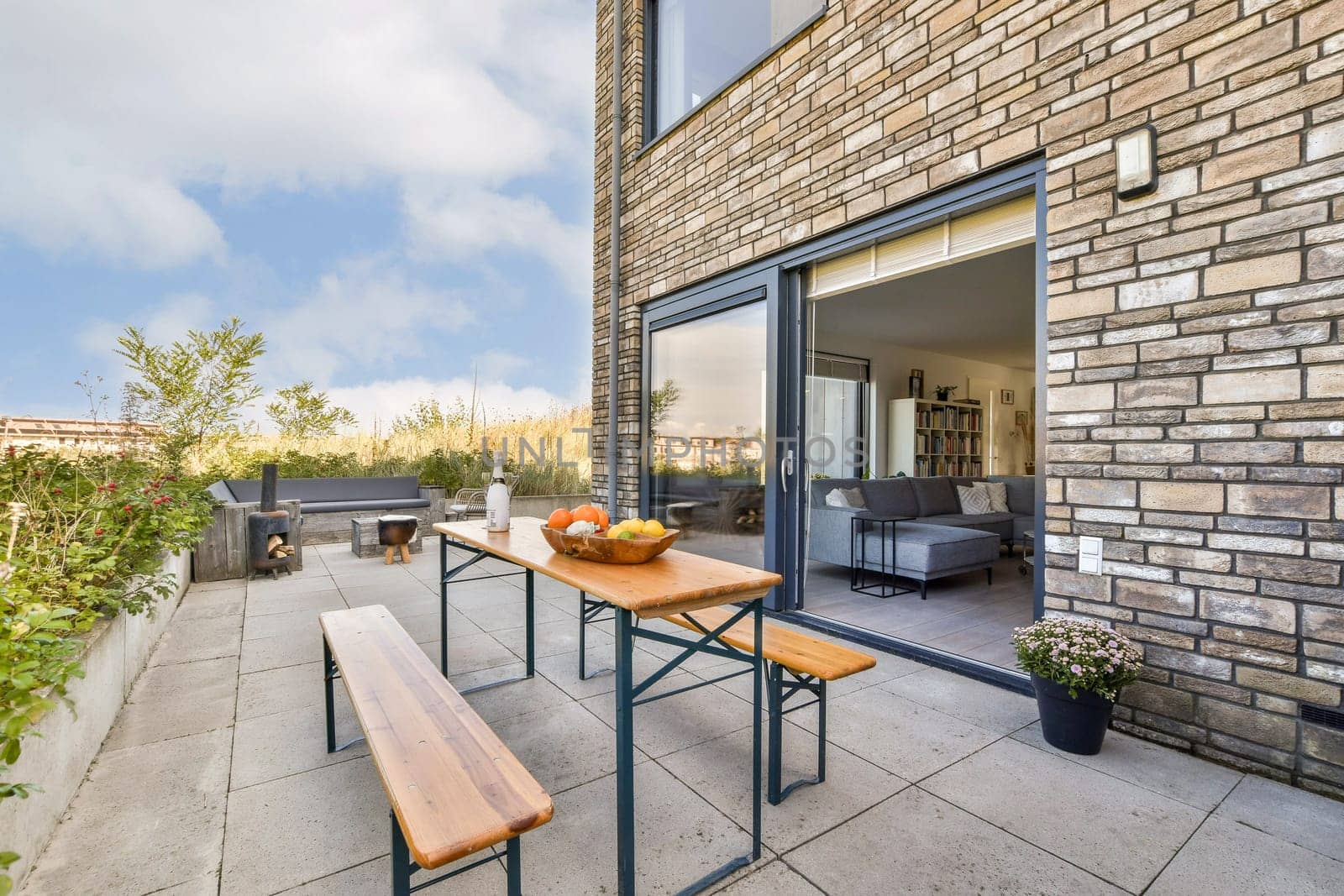 Stylish patio featuring a wooden dining table with fresh fruits, surrounded by greenery and contemporary furniture, ideal for outdoor gatherings.