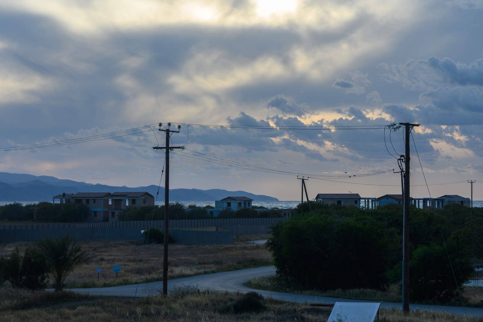 A tranquil coastal landscape unfolds during dusk, with gentle waves lapping against the shore. The sky is filled with soft clouds and a warm golden light. Distant mountains create a serene backdrop.