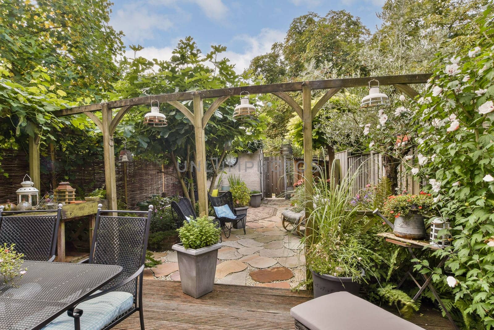 A tranquil garden pathway lined with vibrant plants and a wooden pergola. Decorative lanterns add charm to this peaceful outdoor space, ideal for relaxation.
