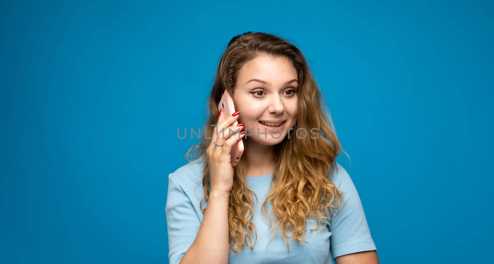 Portrait of a beautiful young woman talking on the phone on blue background