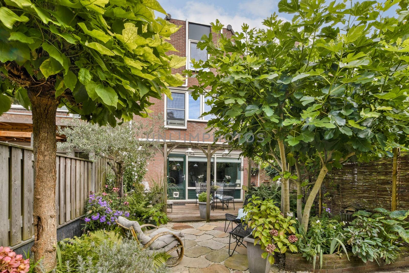 Lush greenery surrounds a cozy patio featuring flowering plants and a rustic seating area, perfect for relaxation and outdoor gatherings.