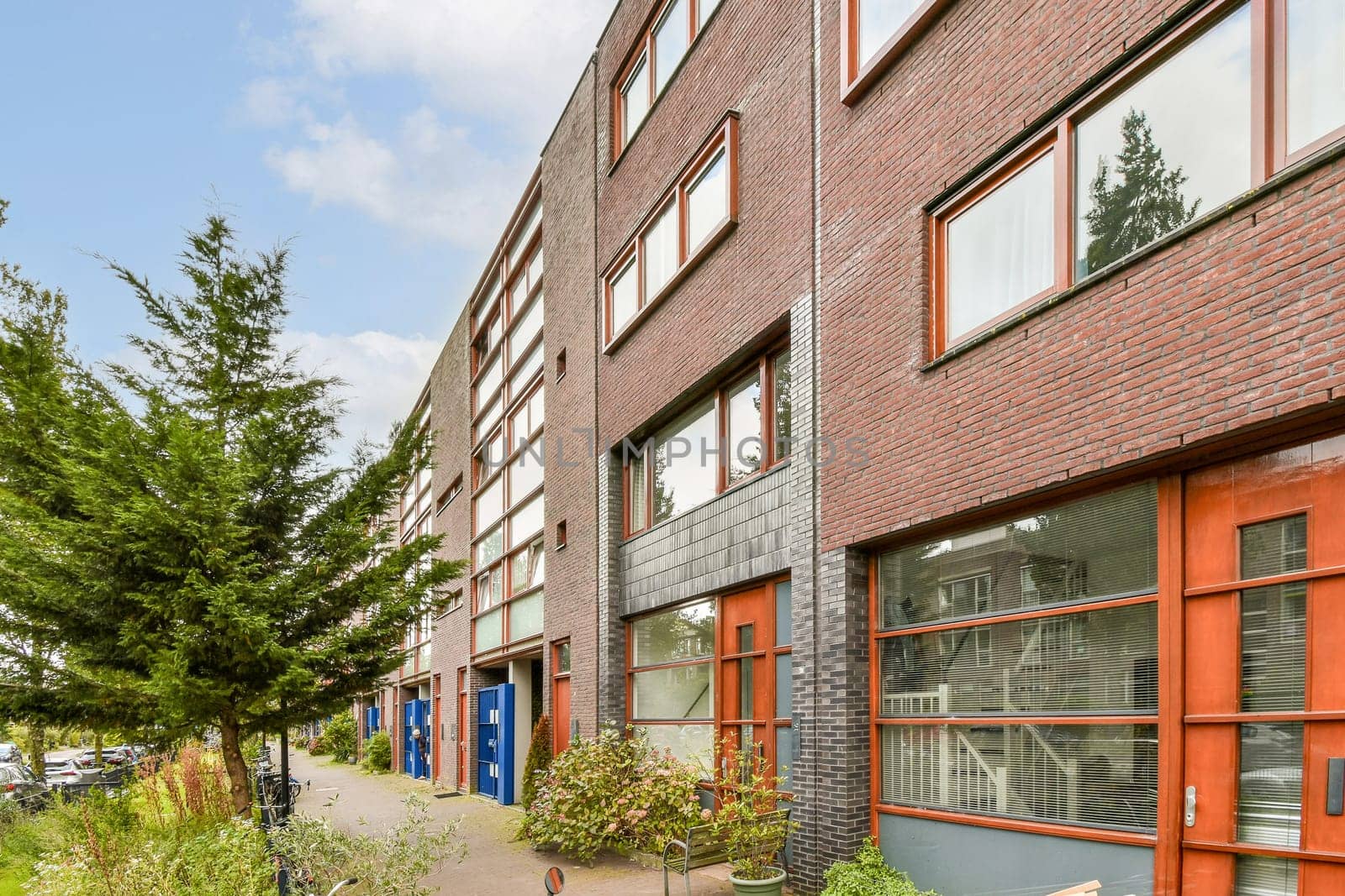 The image showcases a modern urban building with large windows, a stylish exterior, and greenery surrounding the entrance, reflecting contemporary architectural design.