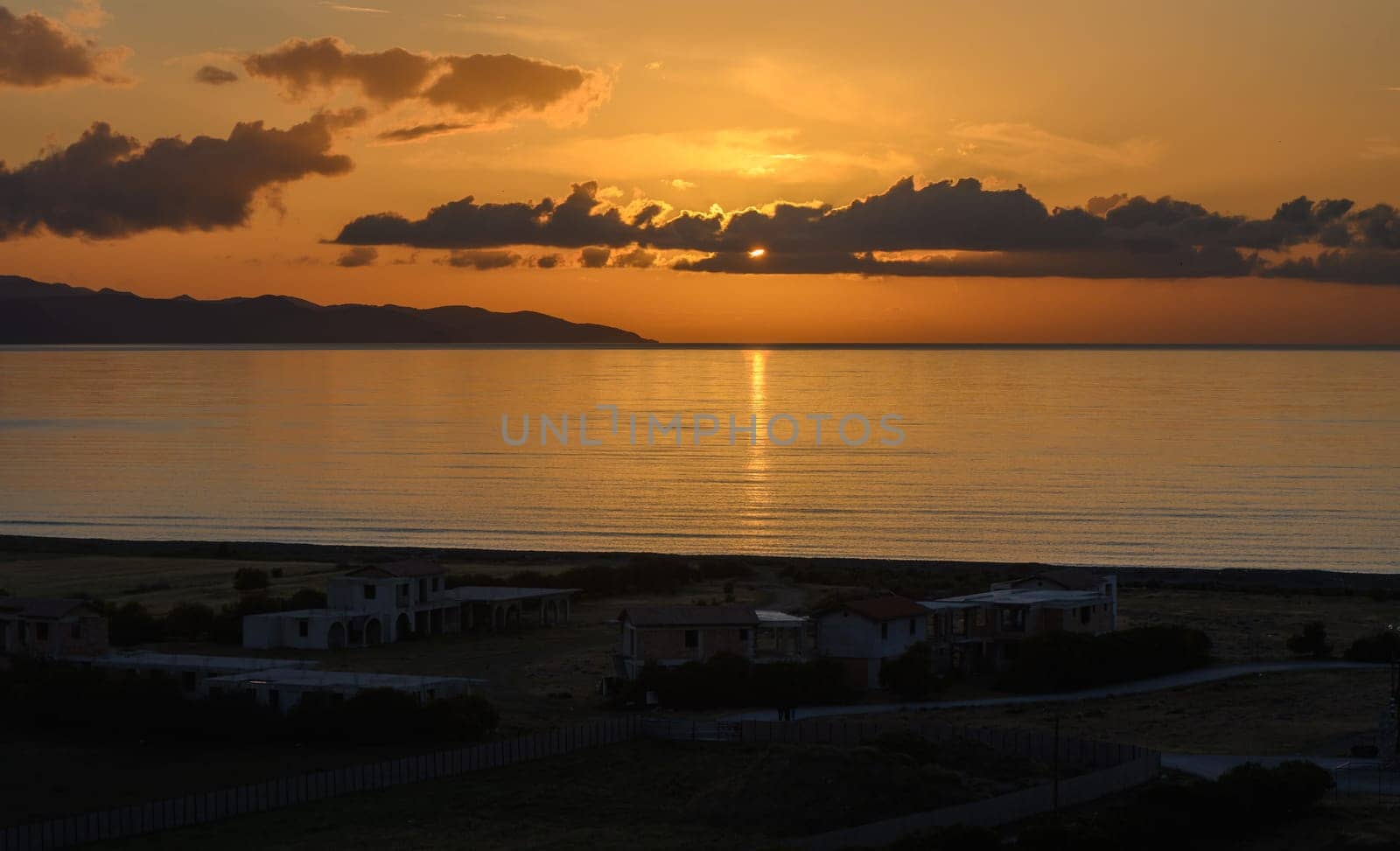 A vibrant sunset paints the sky in hues of orange and gold, as gentle waves lap the shore.