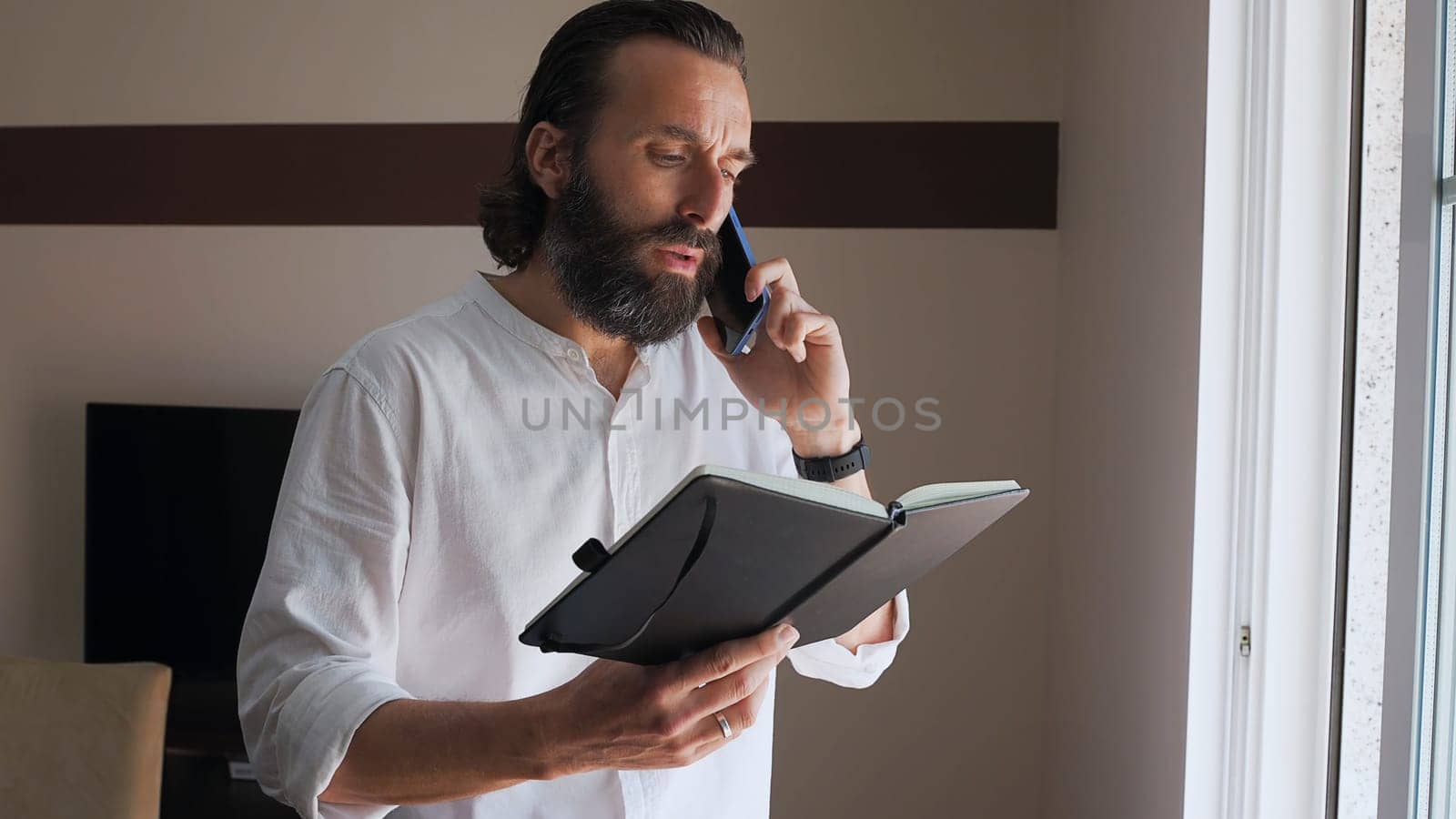 Focused adult man multitasking on a phone call and organizing notes in a modern office space.