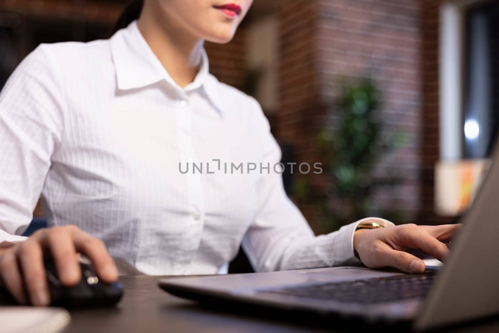 Asian female professional typing diligently on her laptop at her office desk. The closeup shot emphasizes her fingers, showing her focus on data analysis and business reporting in modern workspace.