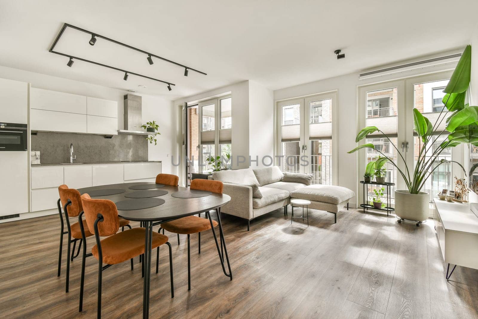 Contemporary living area featuring a sleek dining table, stylish chairs, and large windows for natural light. A green plant adds a touch of nature to the urban setting.