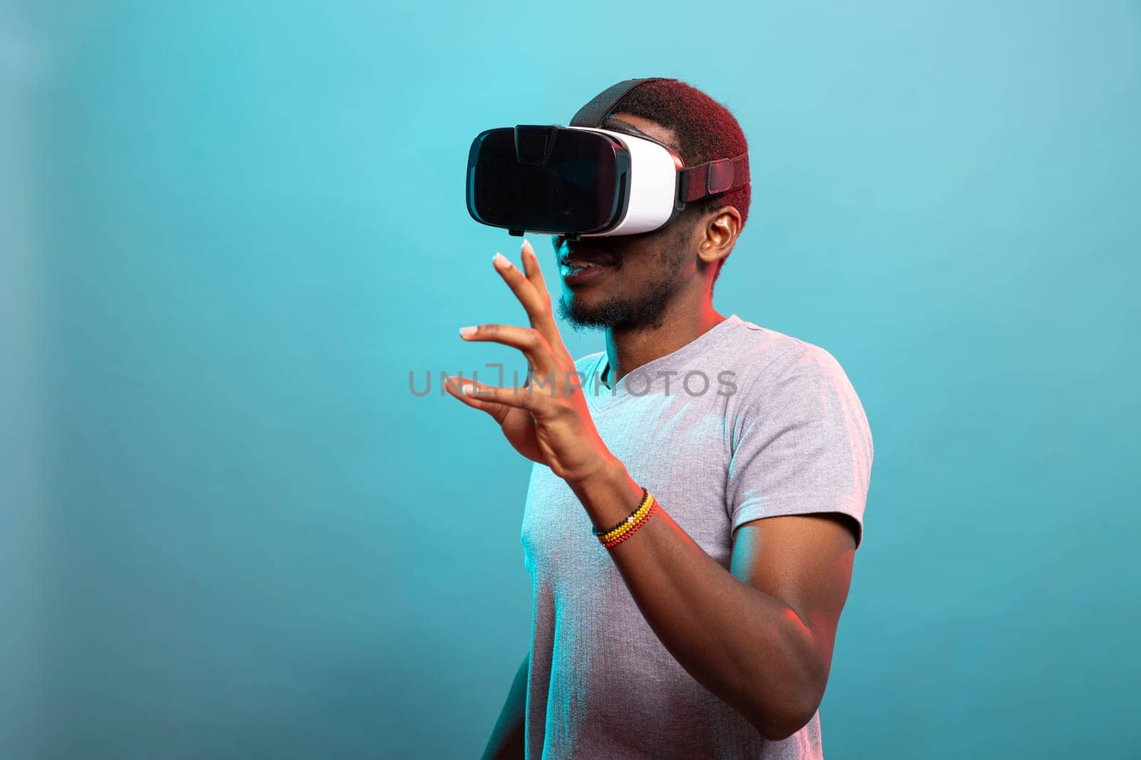 Black man exploring virtual reality, using goggles to interact with futuristic elements. Enthusiastic male gamer wearing VR headset, enjoying immersive technology, fully engaged in a digital world.