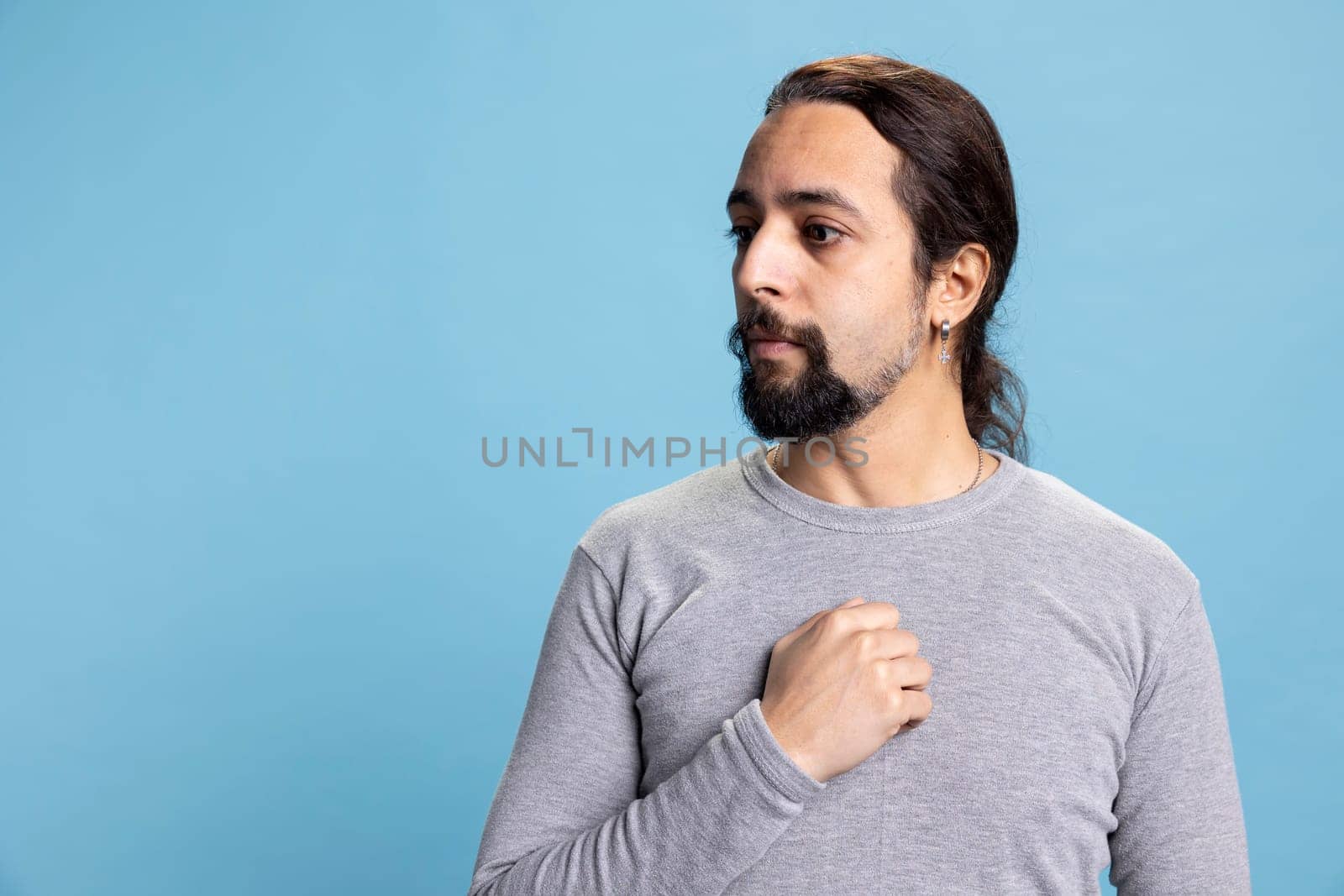Stressed confused worried man feeling shy and insecure with anxious thoughts, overwhelmed unhappy person against blue background. Young guy with panic and fear in his eyes, desolation.