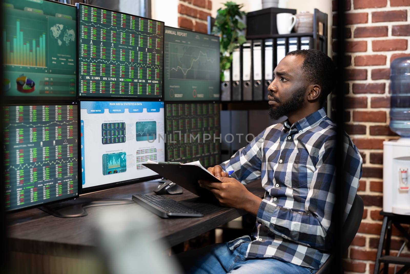 Male stock market trader with a clipboard in hand, analyzing real time data on a multi monitor setup in a dimly lit office. The scene reflects financial analysis and late night investment decisions.
