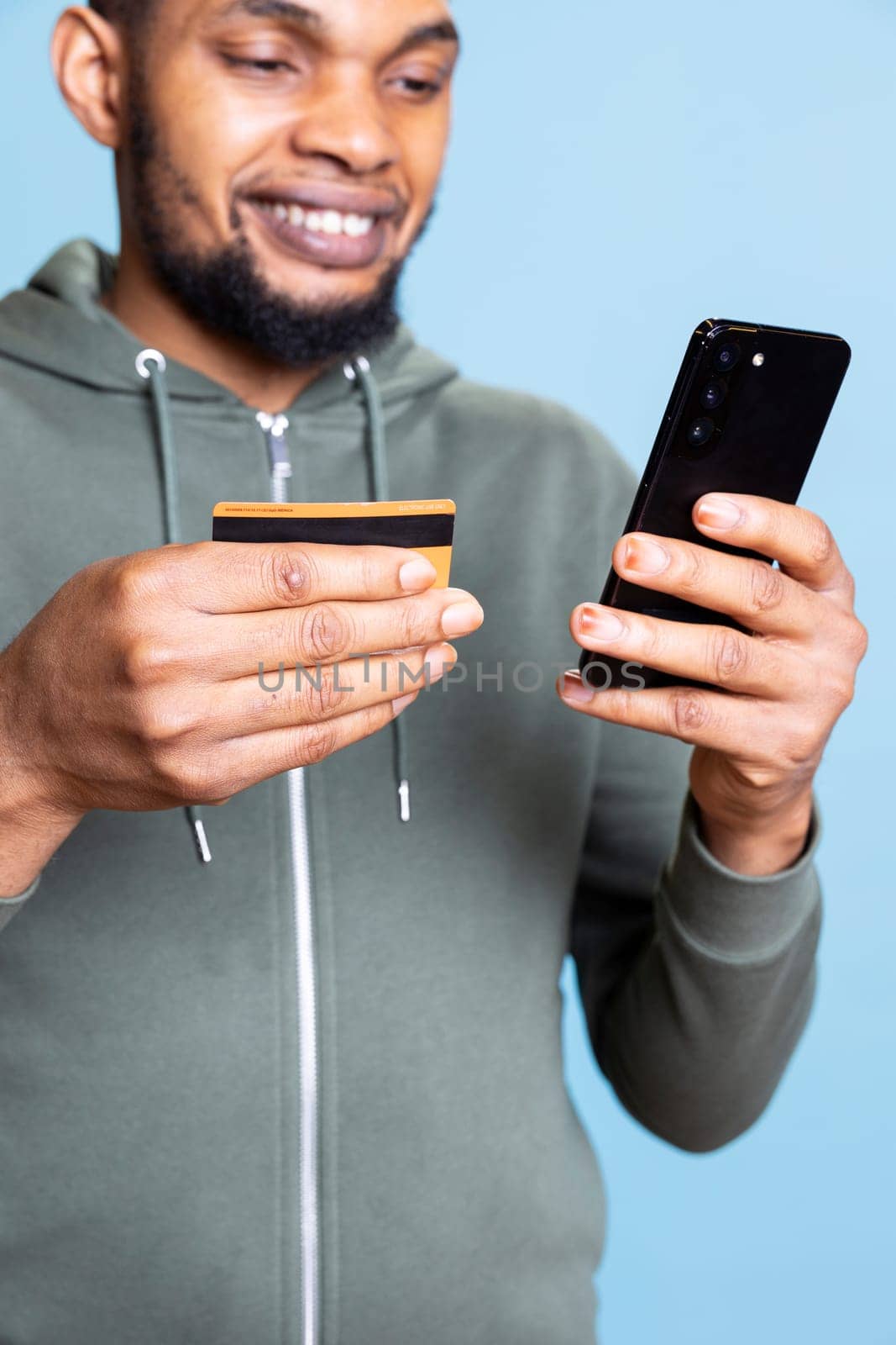 Happy excited african american man making a purchase online with credit card, entering banking credentials to pay for something on promotion. Confident young guy shopping on internet.