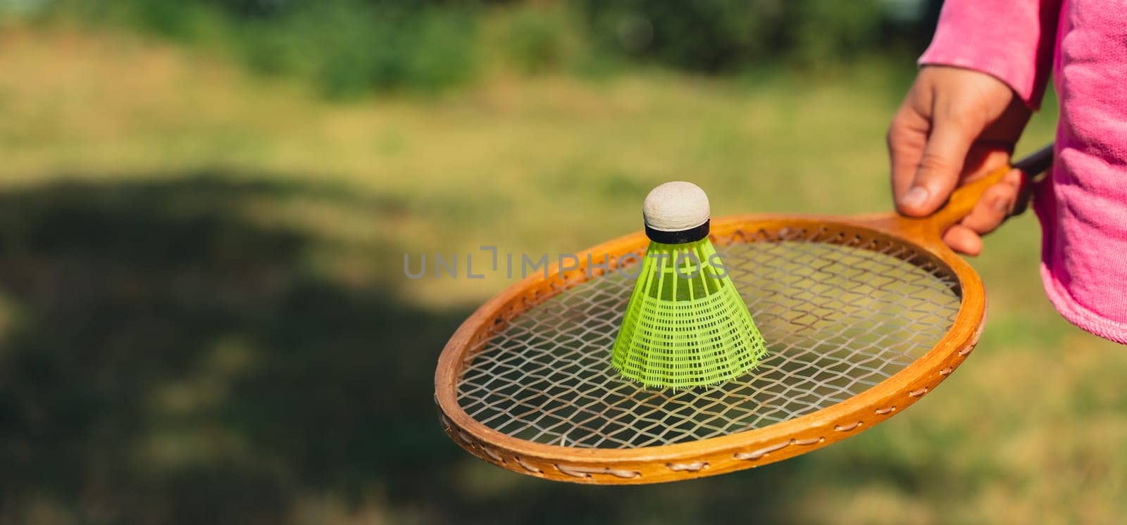 Woman hand holding wooden Badminton racket and shuttlecock. Outside recreation and fresh air. Healthy lifestyle nature connection sport summer activities. Stress relief hobby healthcare