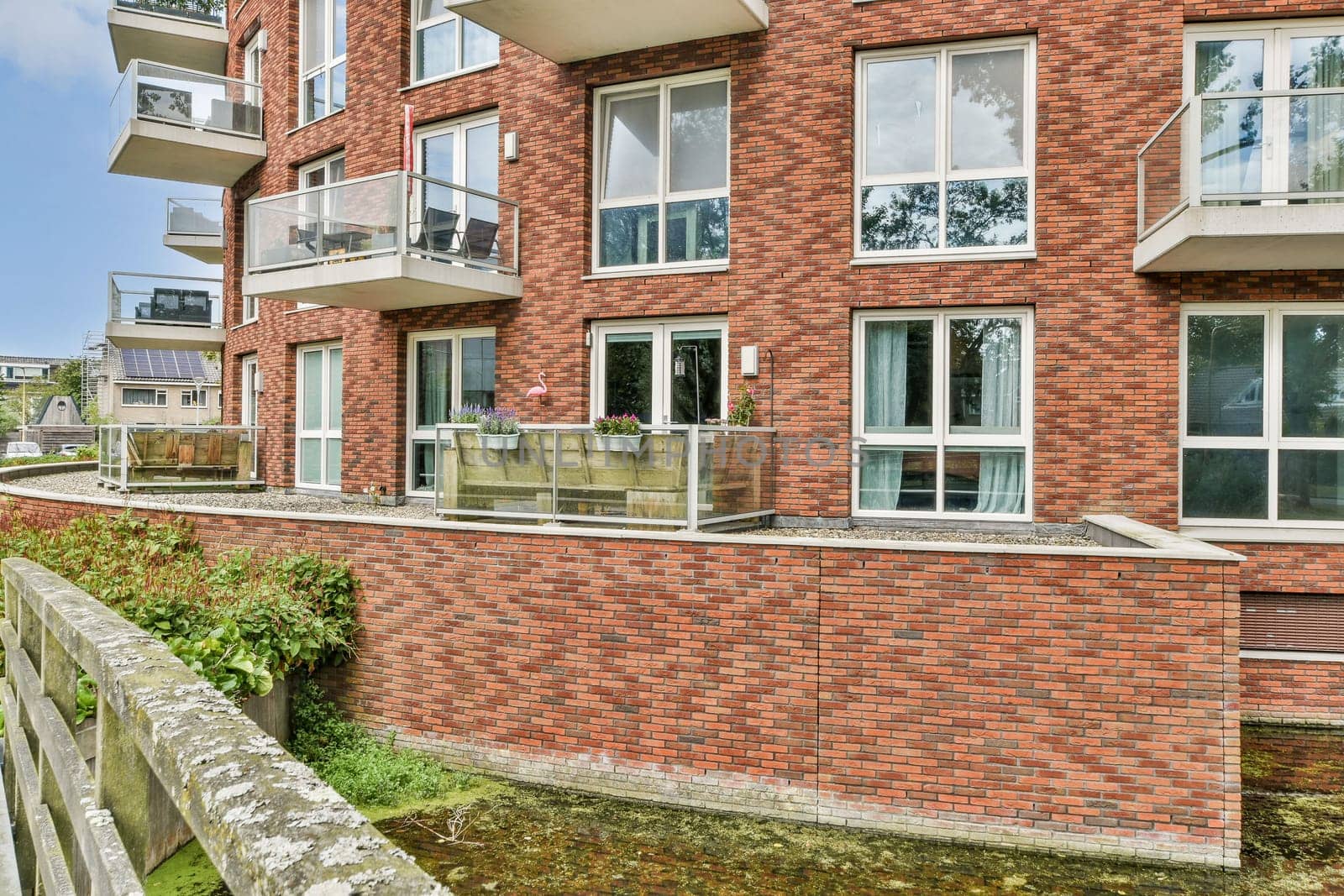 A contemporary apartment complex featuring multiple balconies, large windows, and a mix of brick and modern design elements in a lush urban setting.
