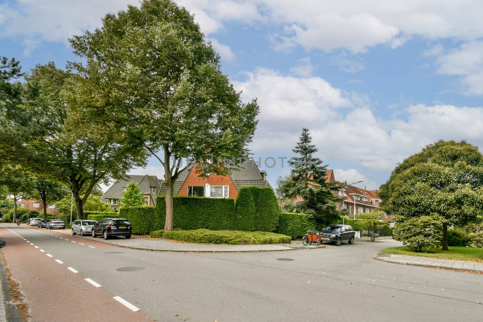 A picturesque view of a serene residential street featuring lush greenery, well-kept homes, and parked cars under a partly cloudy sky.