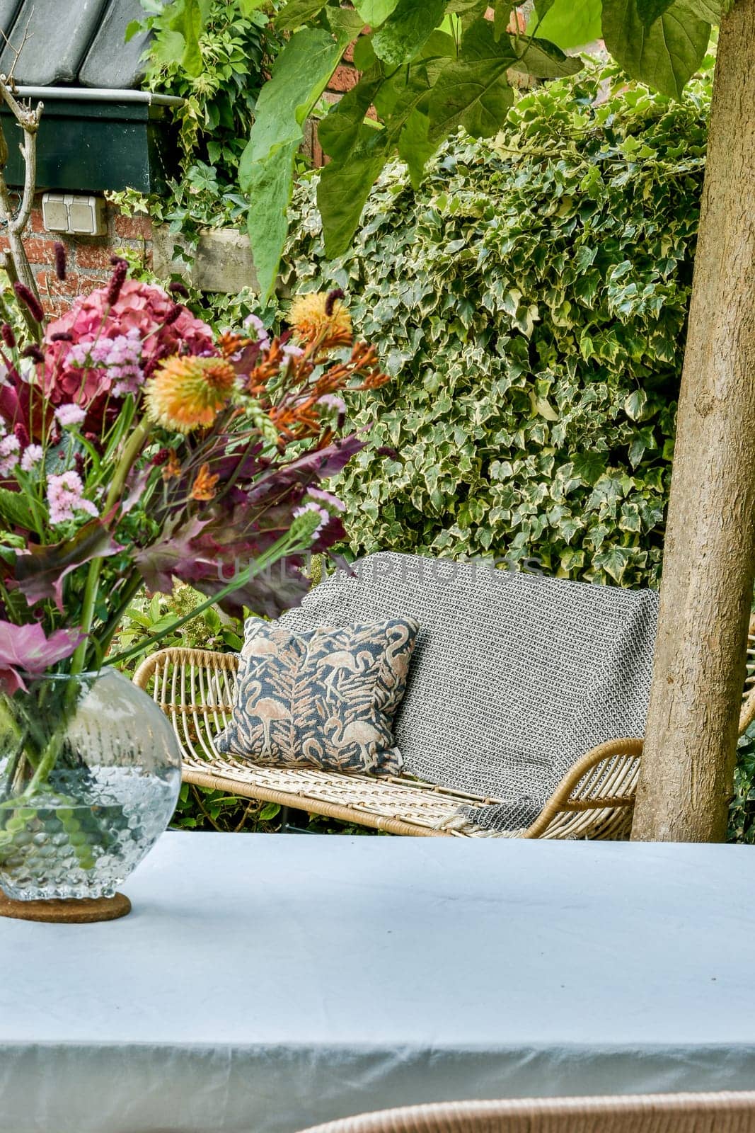 A beautifully arranged bouquet of flowers in a clear vase sits on a table surrounded by lush greenery and a comfortable seating area.