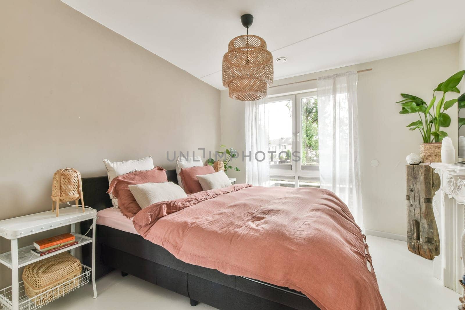 A stylish bedroom featuring a comfortable bed, soft bedding, and natural light illuminating the space. Green plants add a touch of freshness to the decor.