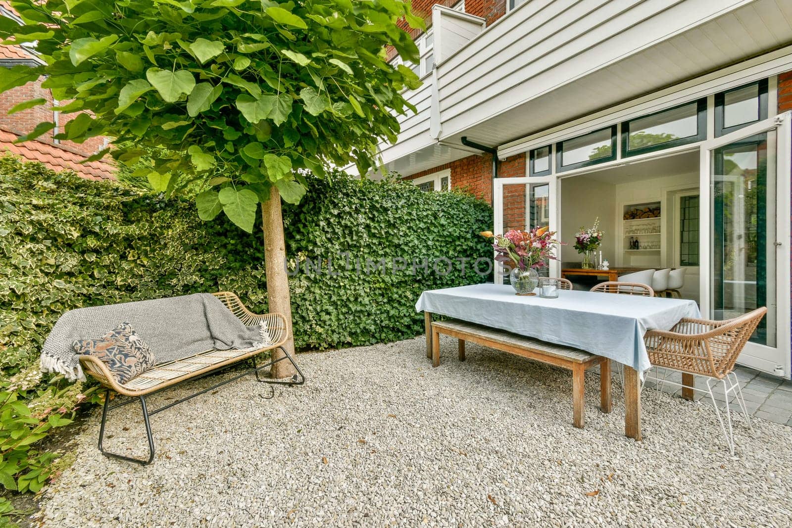 A beautifully designed outdoor patio featuring greenery, a table set for dining, and comfortable seating, providing a serene space for relaxation.