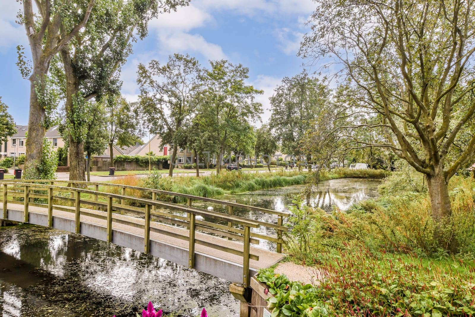 A peaceful park scene featuring a wooden bridge over a calm waterway, enhancing the tranquility of the lush greenery surrounding it.