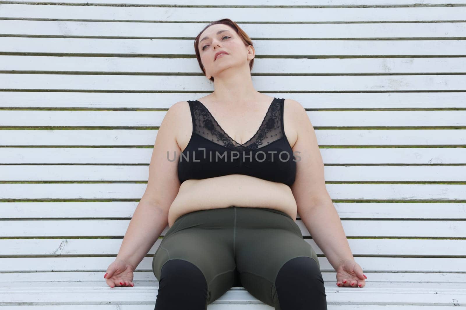 Fat woman with cellulite is tired after fitness. Woman sitting on a white bench in a relaxed pose.