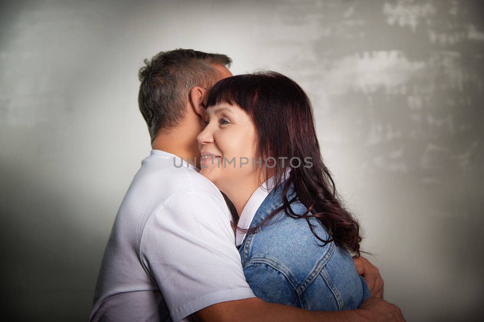 A middle-aged couple embraces warmly indoors, capturing their deep affection for each other in a cozy apartment setting.