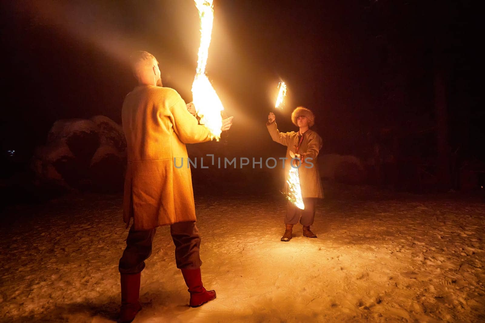 Actors dressed as Vikings perform a thrilling fire show under a clear, starry sky during a cold winter night.