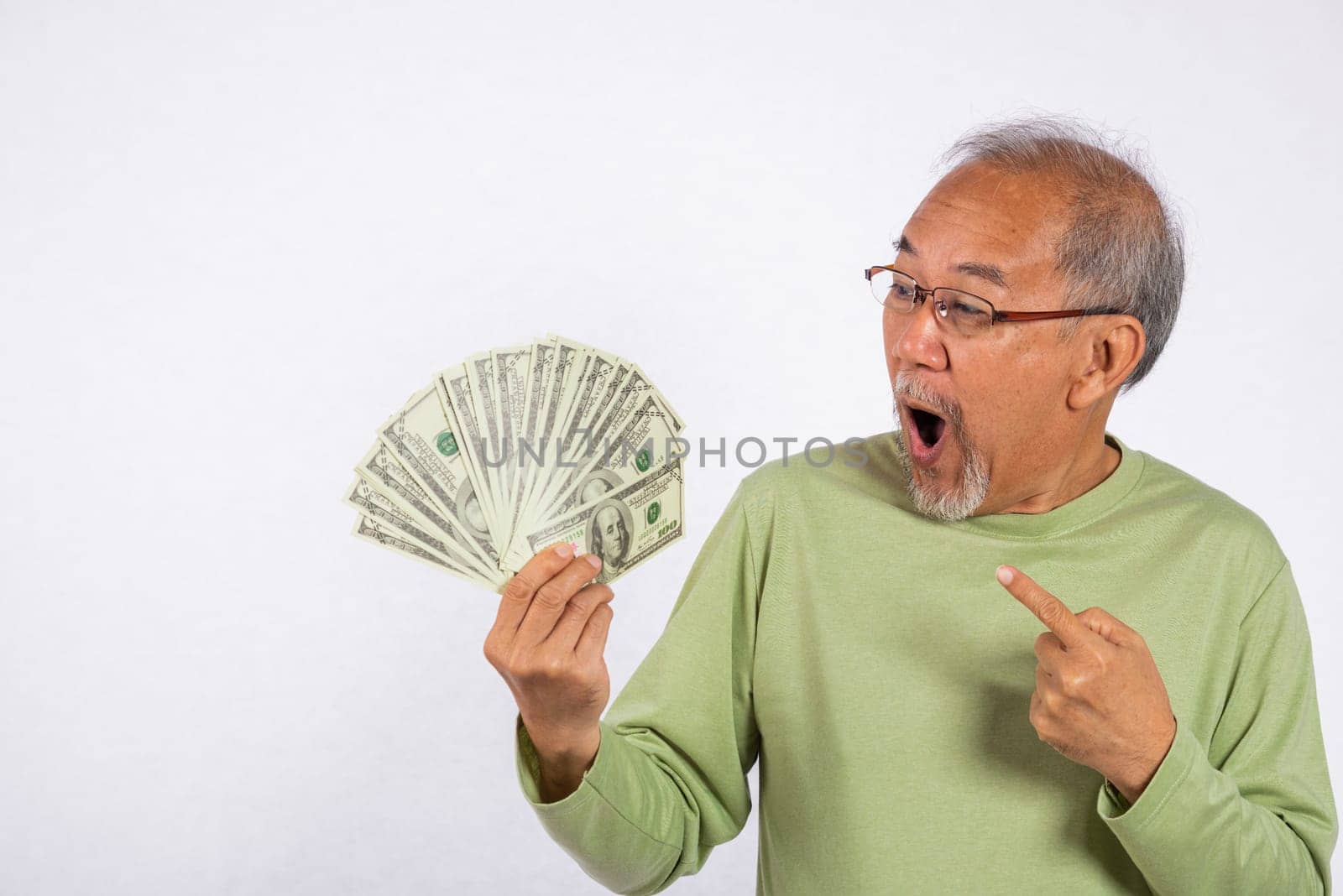 Portrait Asian smiling old man is holding a bunch of money banknotes and pointing studio shot isolated on white background. happy elderly positive excited hold dollar banknotes fan, Financial success