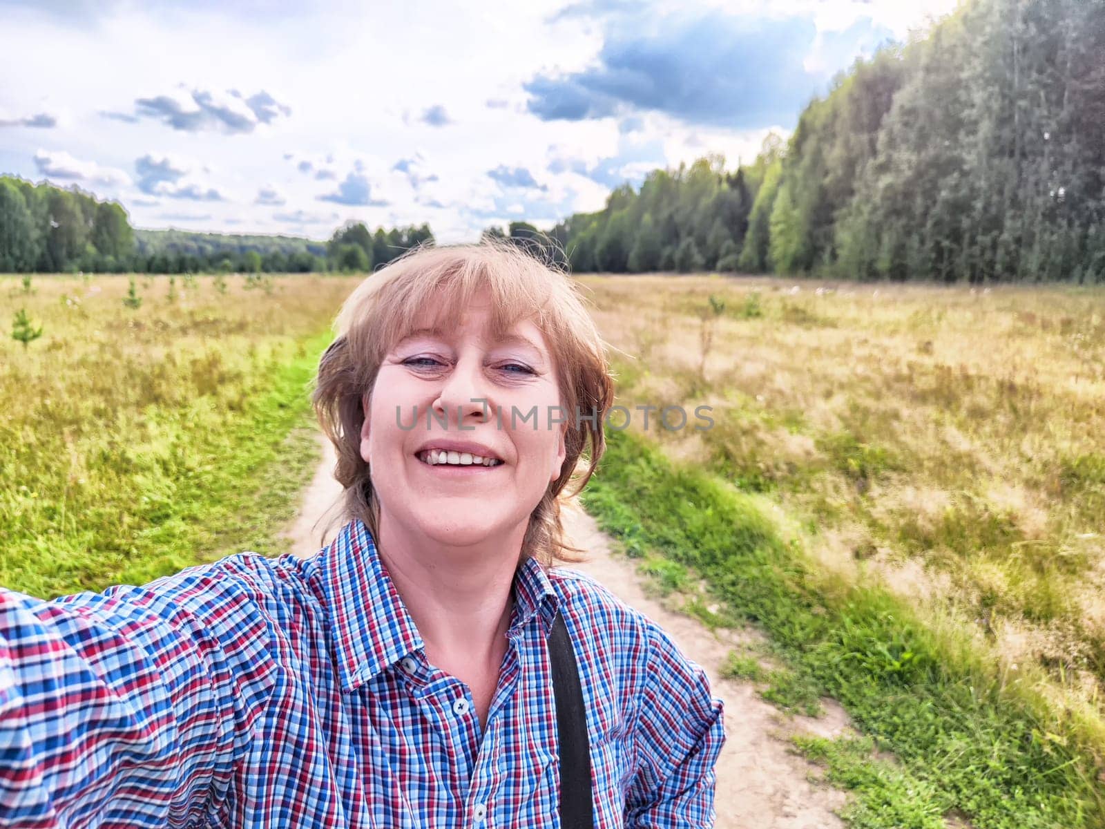 A blonde traveler blogger takes a cheerful selfie in a lush landscape during her outdoor adventure in nature.