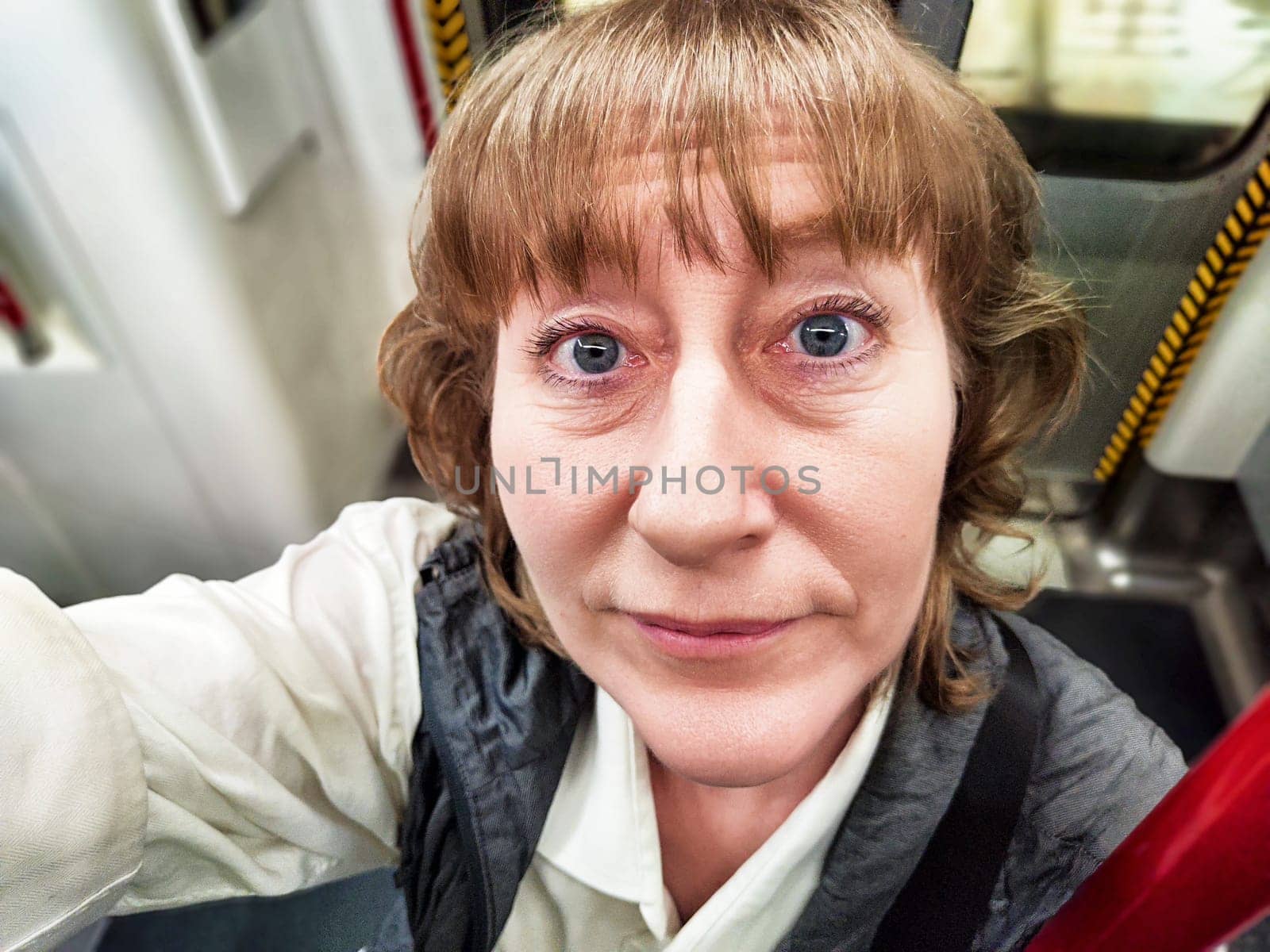A middle-aged woman with blonde hair captures a selfie while riding the subway, enjoying her urban exploration and travel experience.