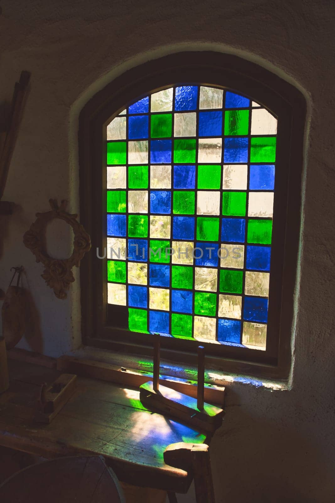 Colorful stained glass window in historical surroundings. Play of light on rustic wooden table with antique tools. Nostalgic atmosphere in vintage style