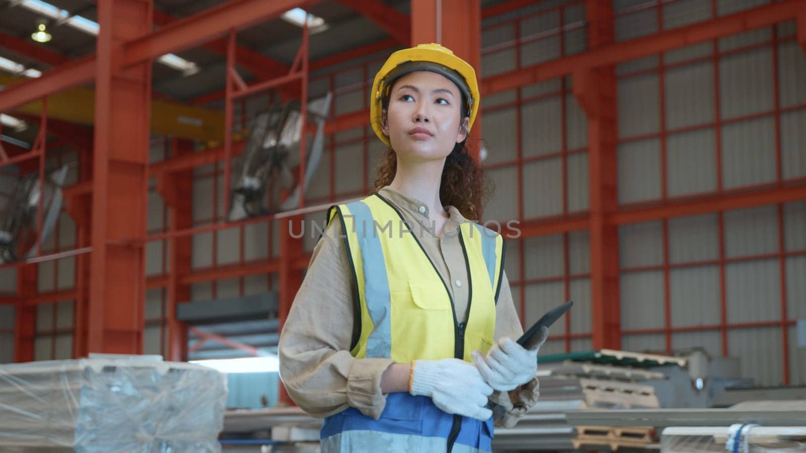Asian worker woman with safety vest holding tablet computer walking to checking warehouse storage in factory, Professional engineer checking machine walk at roofing metal sheet storage industrial