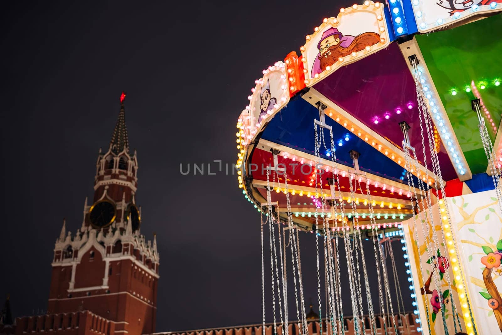 Brightly illuminated carousel spinning in front of the Spasskaya Tower of the Moscow Kremlin at night during Christmas holidays
