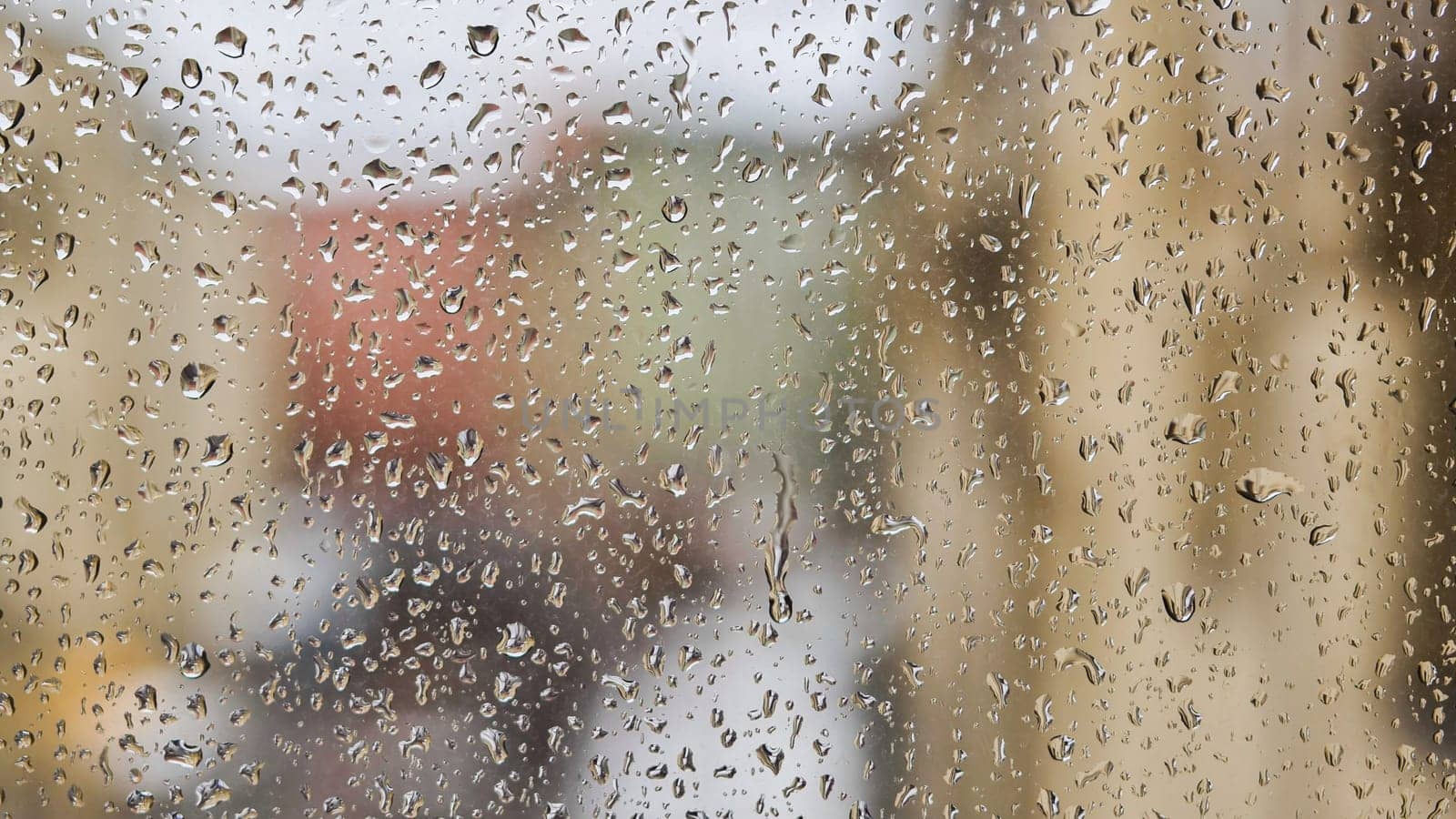 Transparent raindrops sliding on window glass during rainy day blurring city buildings in background, creating abstract pattern