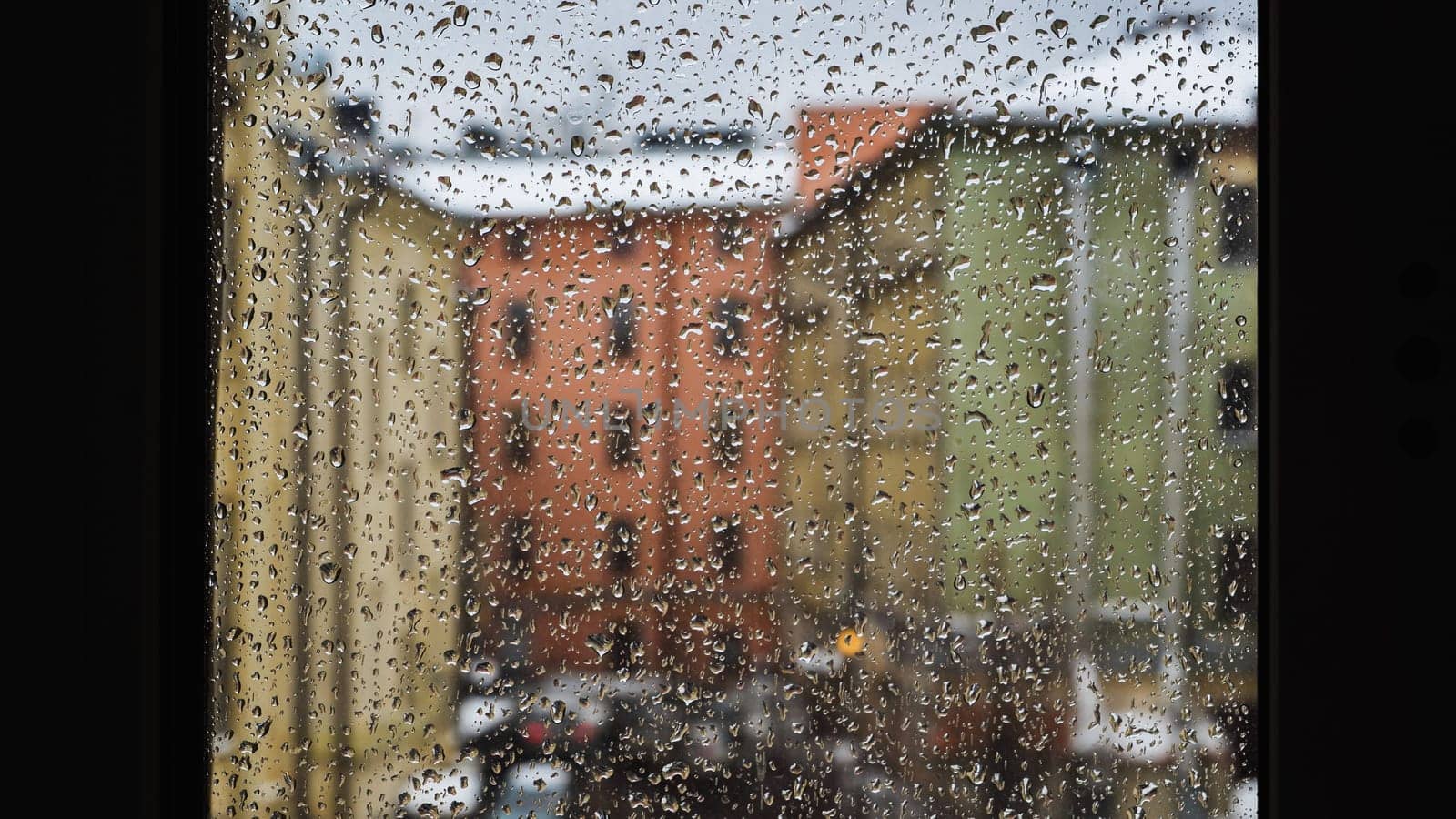 Raindrops sliding on window glass blurring buildings in the background creating an abstract texture