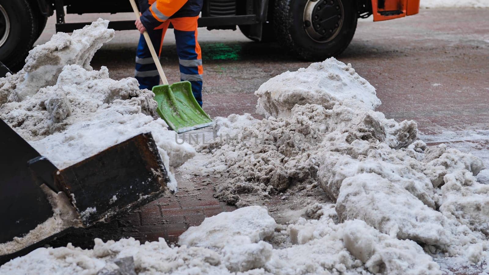 Road worker cleaning snow from street with shovel and truck in winter
