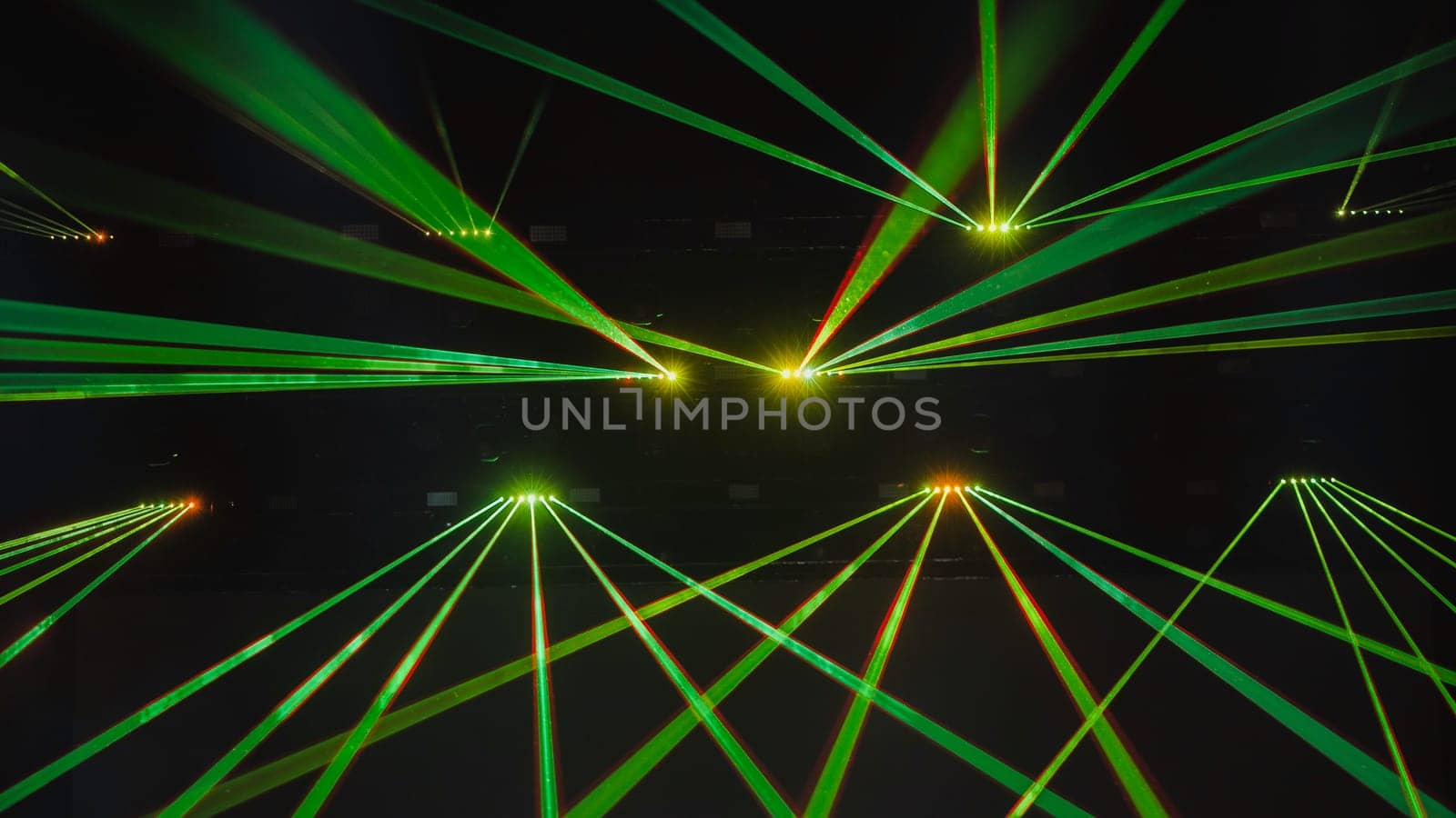 Green laser lights are crossing the darkness of a concert hall during a music festival